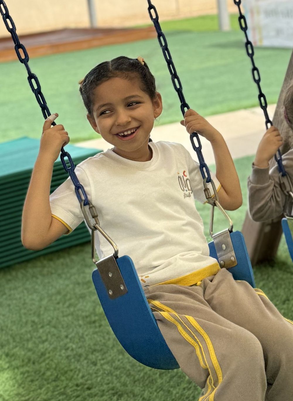 A little girl is sitting on a swing and smiling.