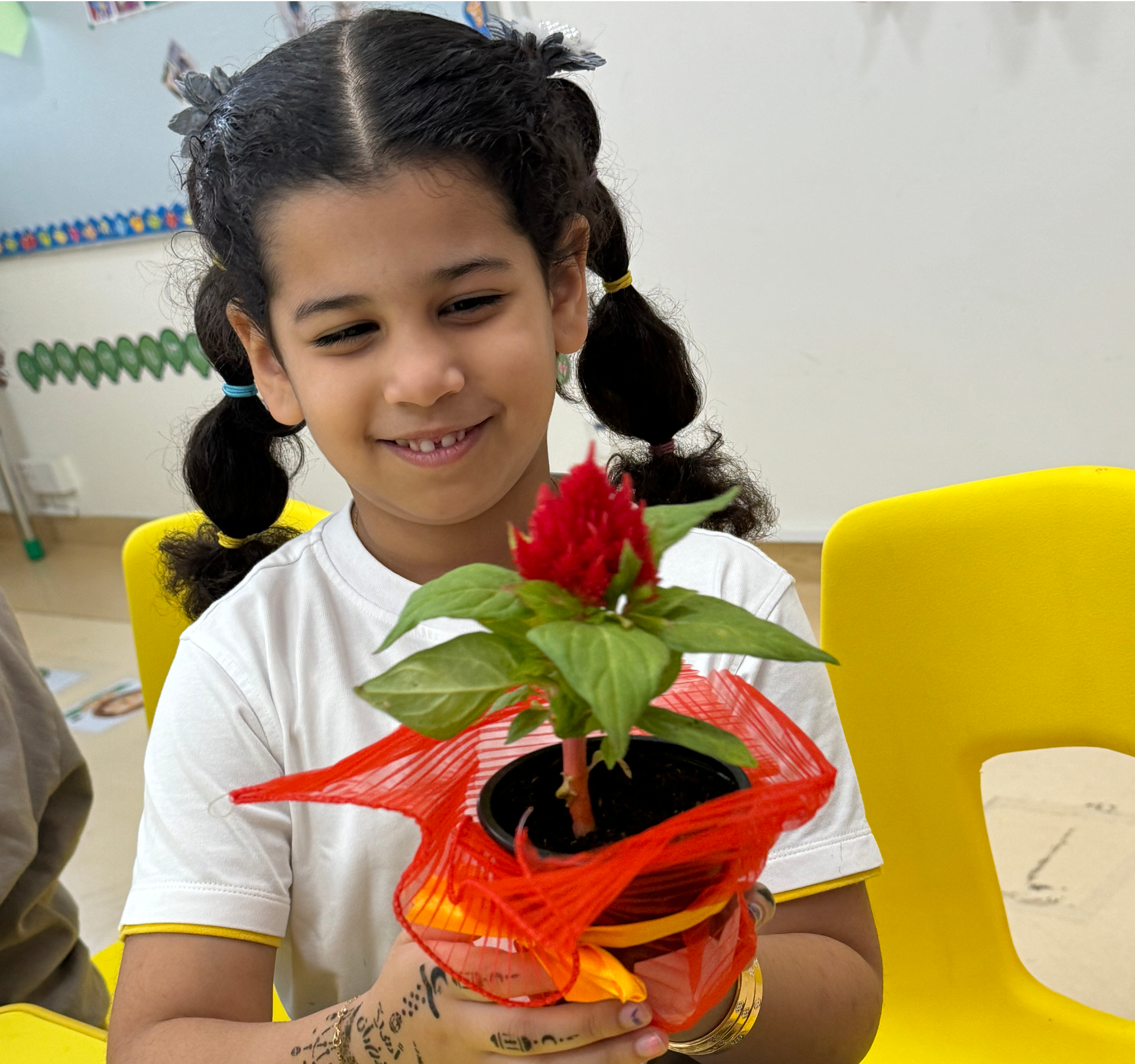 A little girl is sitting at a table holding a potted plant.