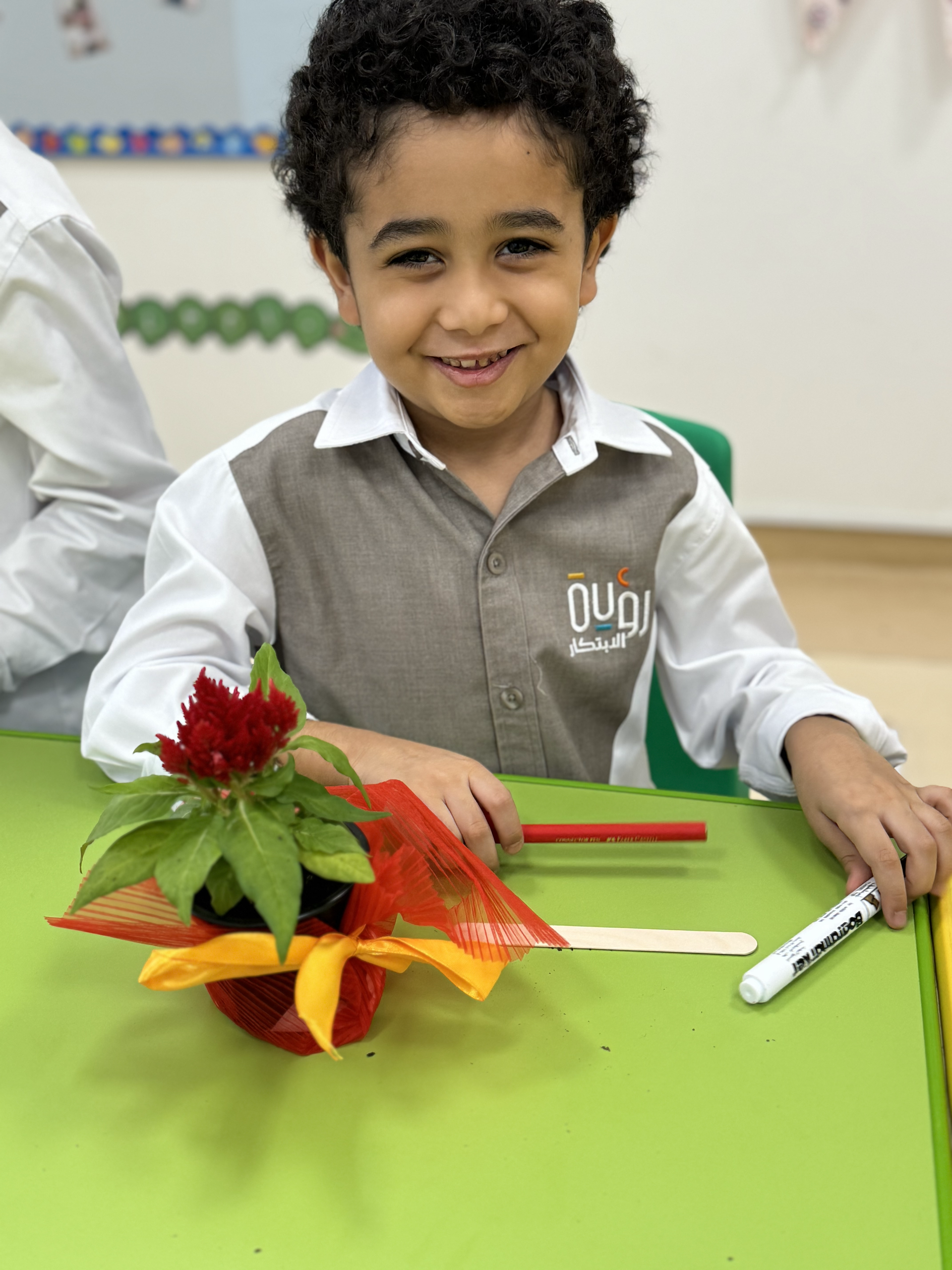 A young boy is sitting at a table with a potted plant and a marker.