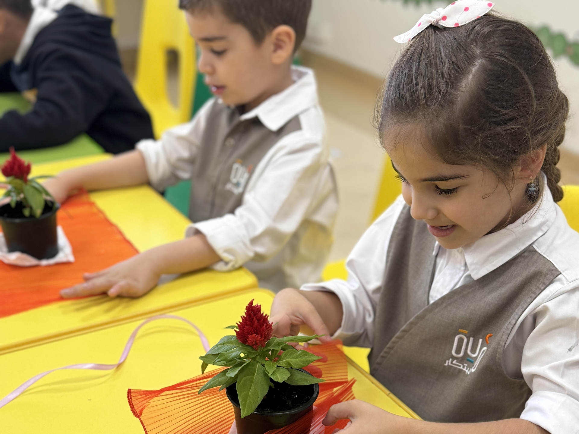 A boy and a girl are sitting at a table with potted plants.