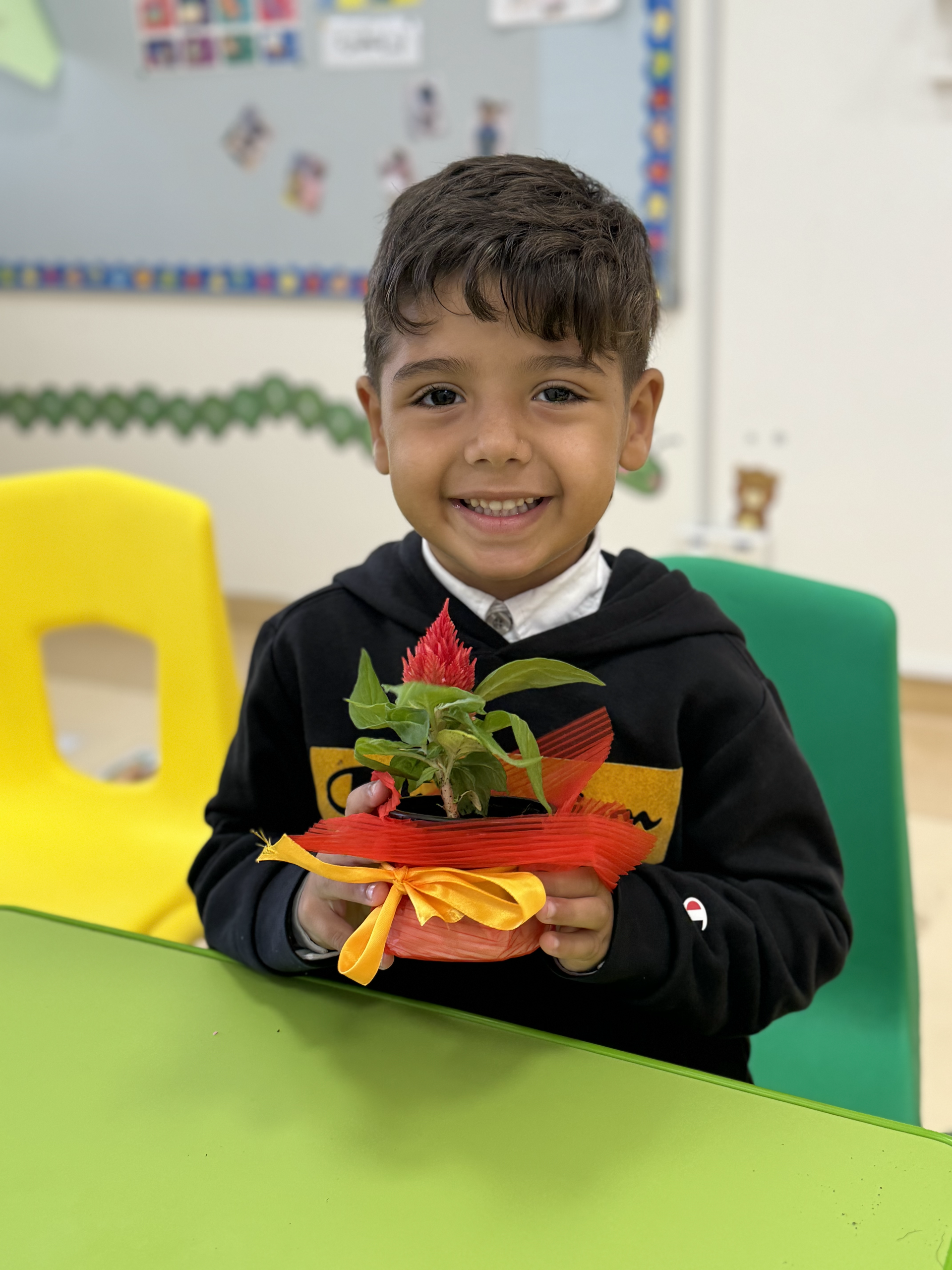 A young boy is sitting at a table holding a potted plant.