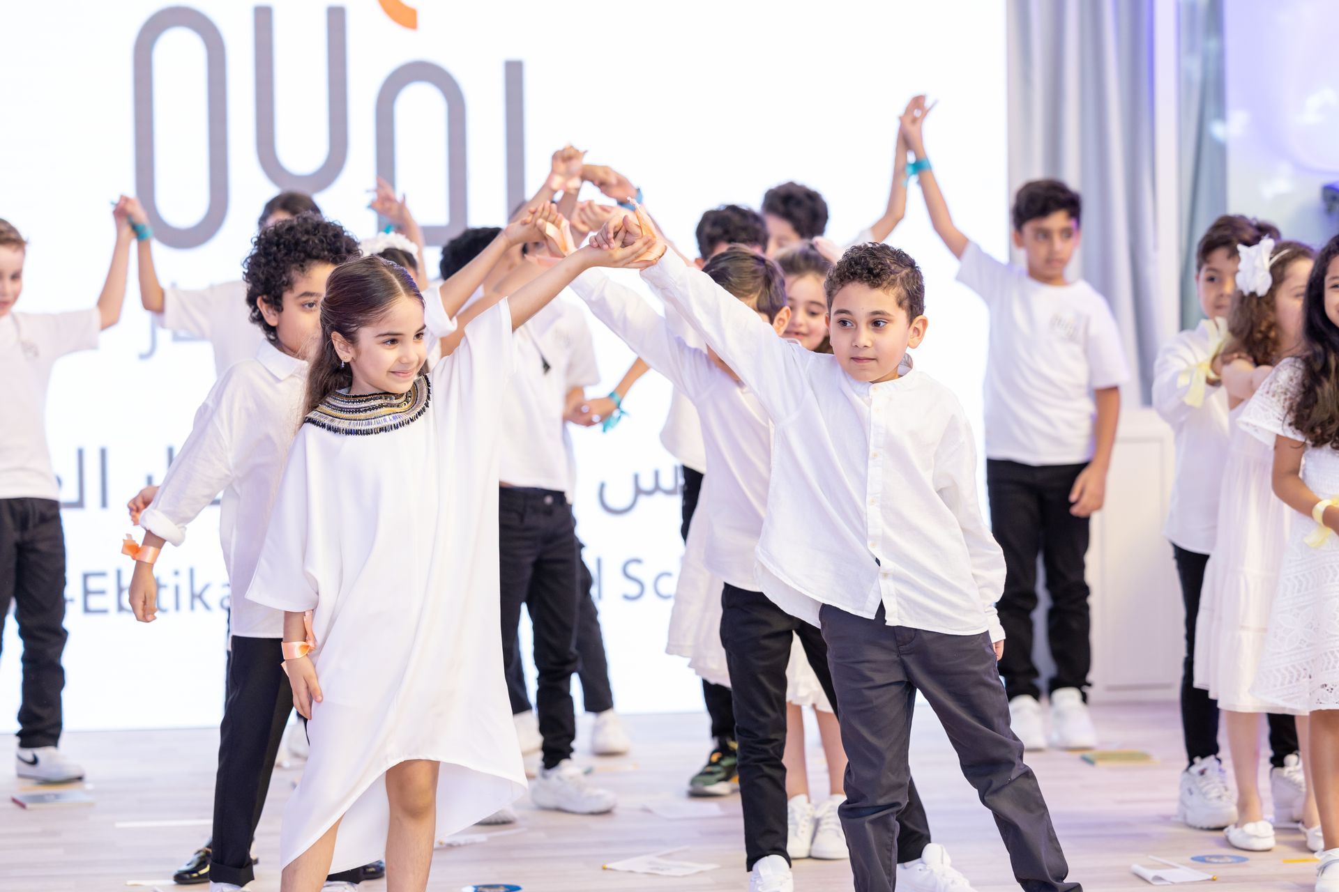 A group of children are dancing together in front of a large screen.