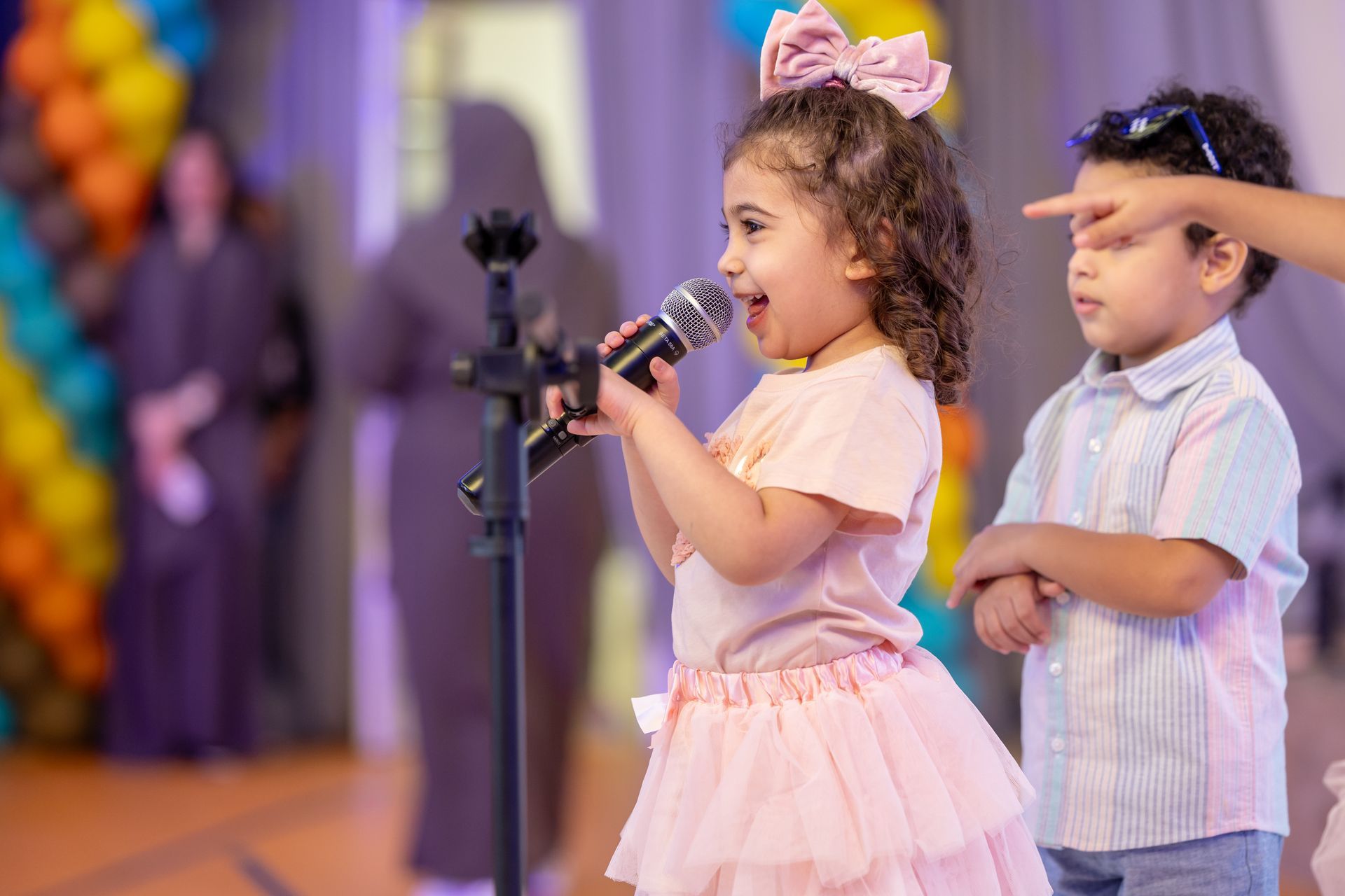 A little girl is singing into a microphone while standing next to a boy.