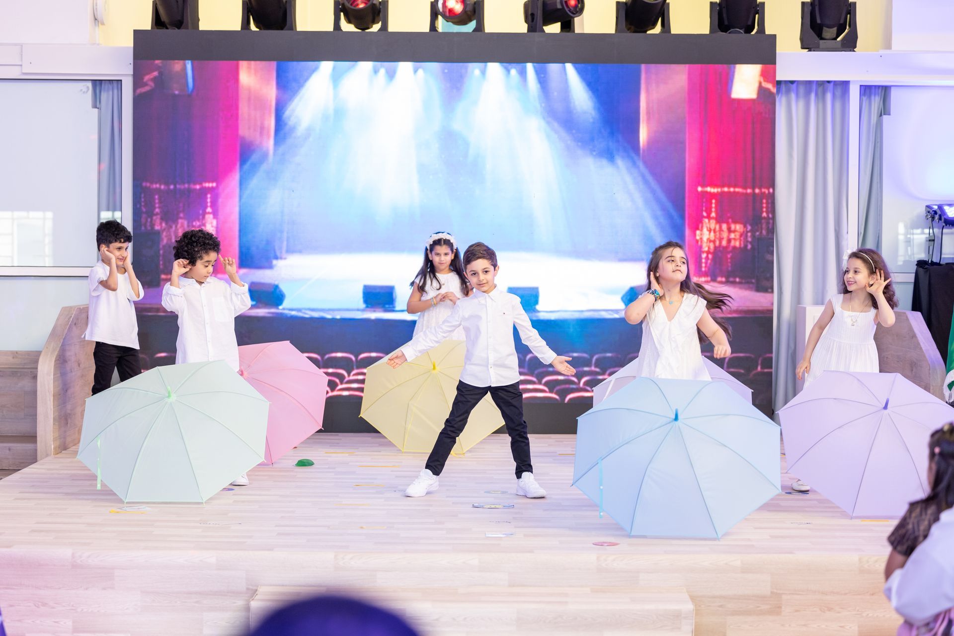 A group of children are dancing on a stage with umbrellas.