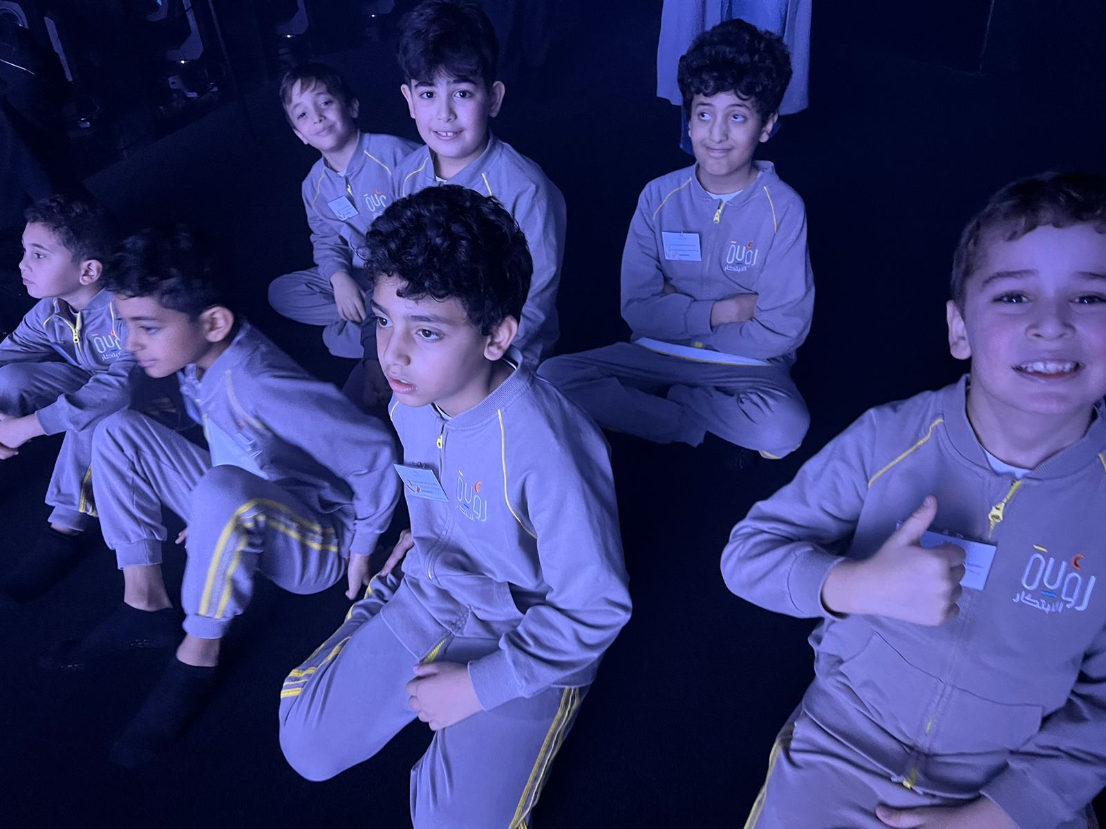 A group of young boys are sitting on the floor giving a thumbs up.