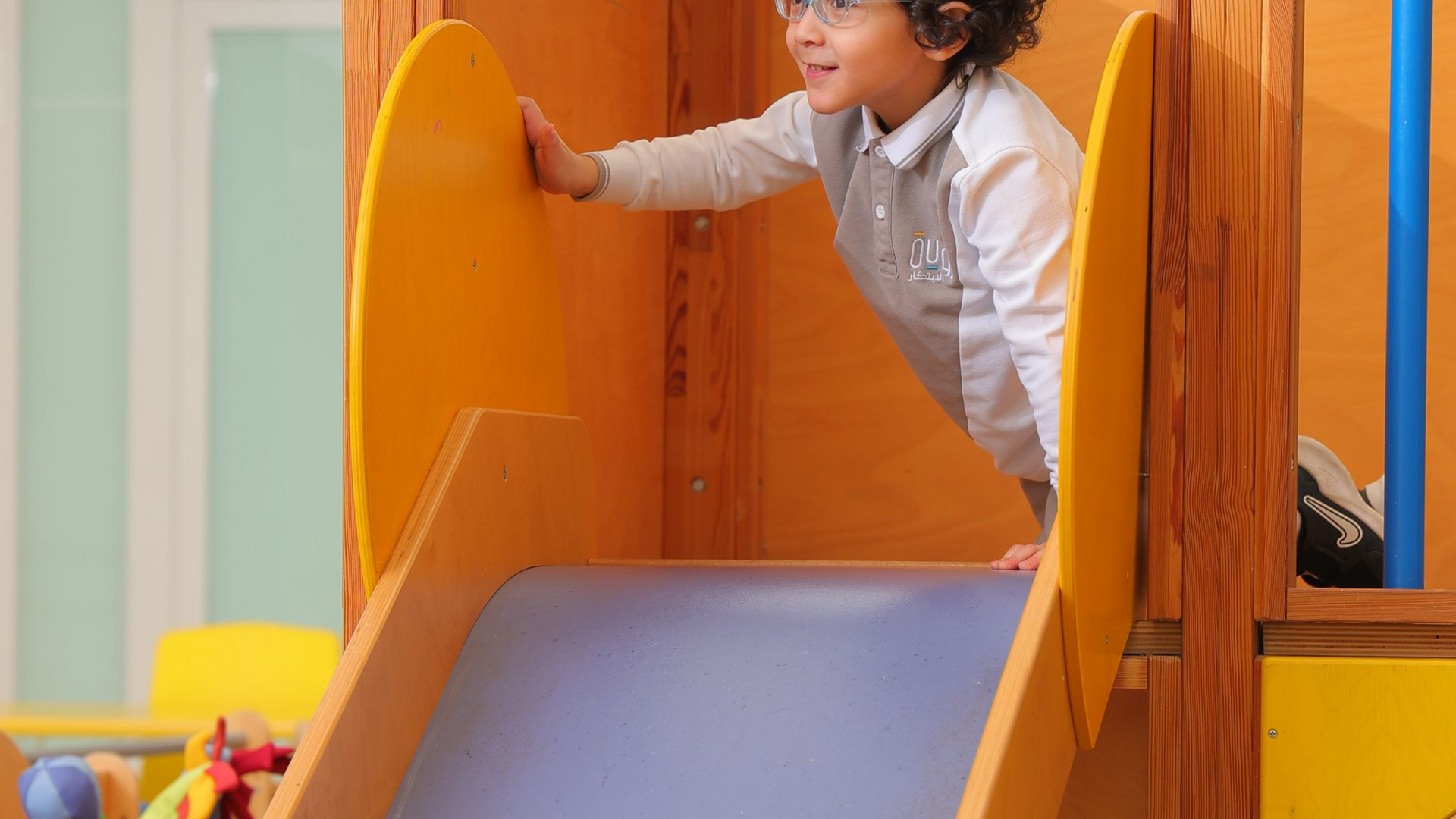 Child playing on a wooden slide in an indoor play area