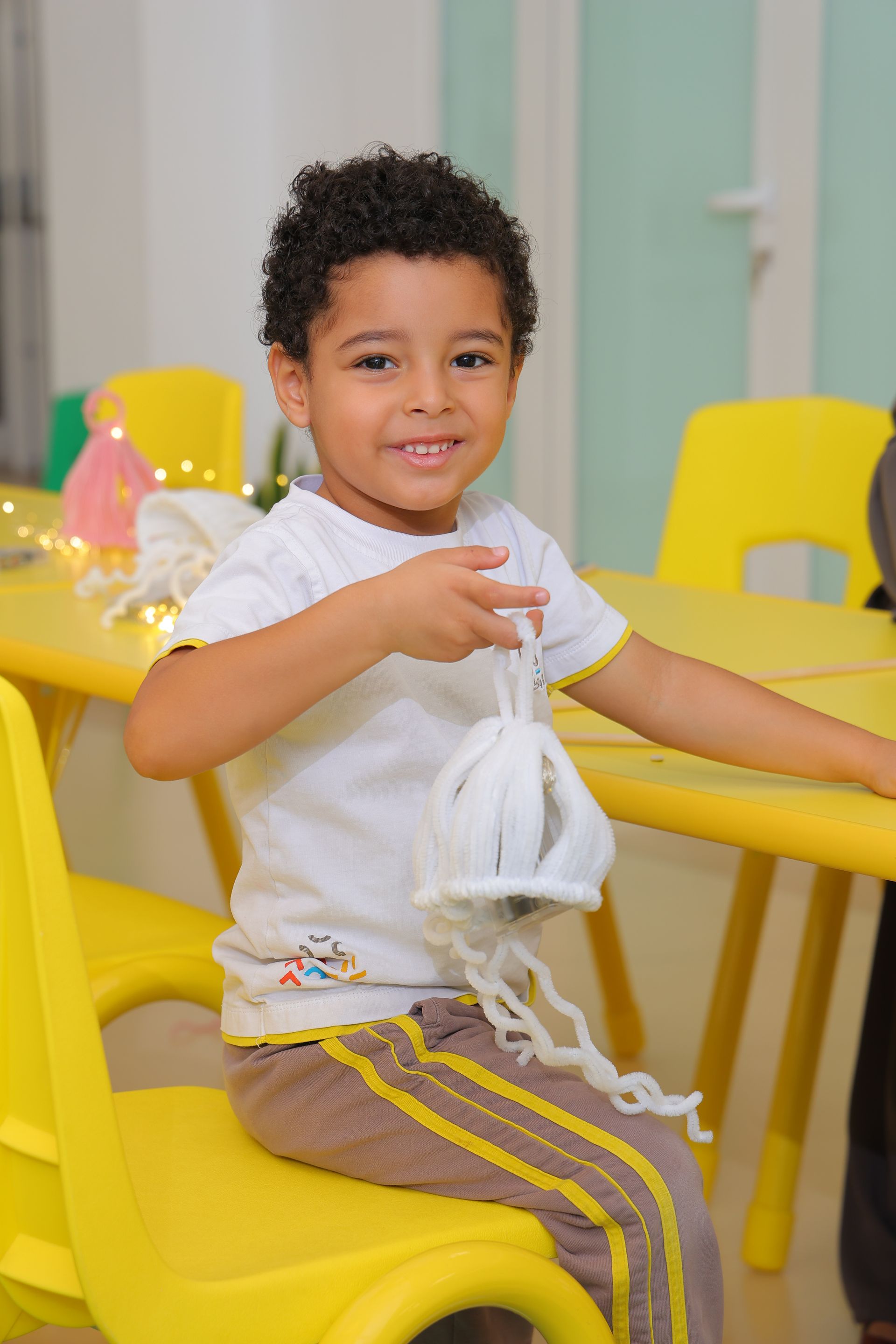 A young boy is sitting at a table holding a cardboard house.