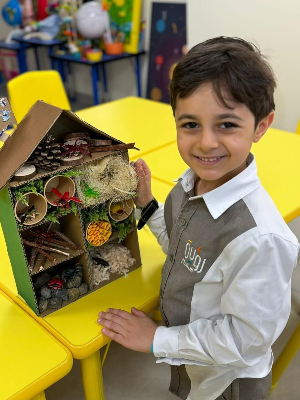 A young boy is sitting at a table holding a cardboard house.