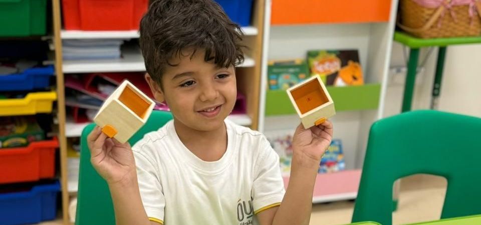 A young boy is sitting at a table holding two wooden blocks.
