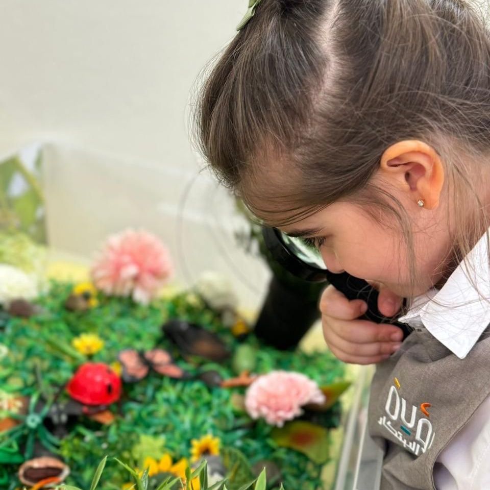 A little girl is looking through a magnifying glass at flowers.