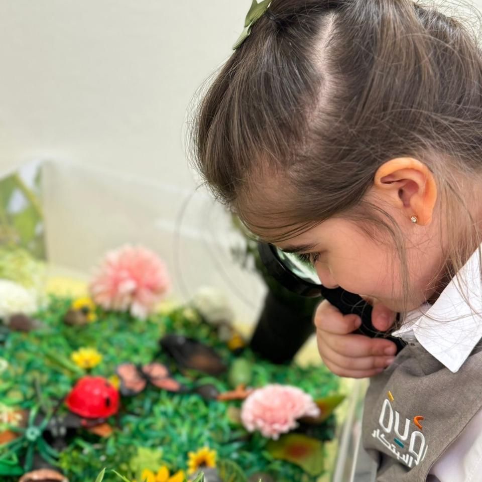 A little girl is looking through a magnifying glass at flowers.