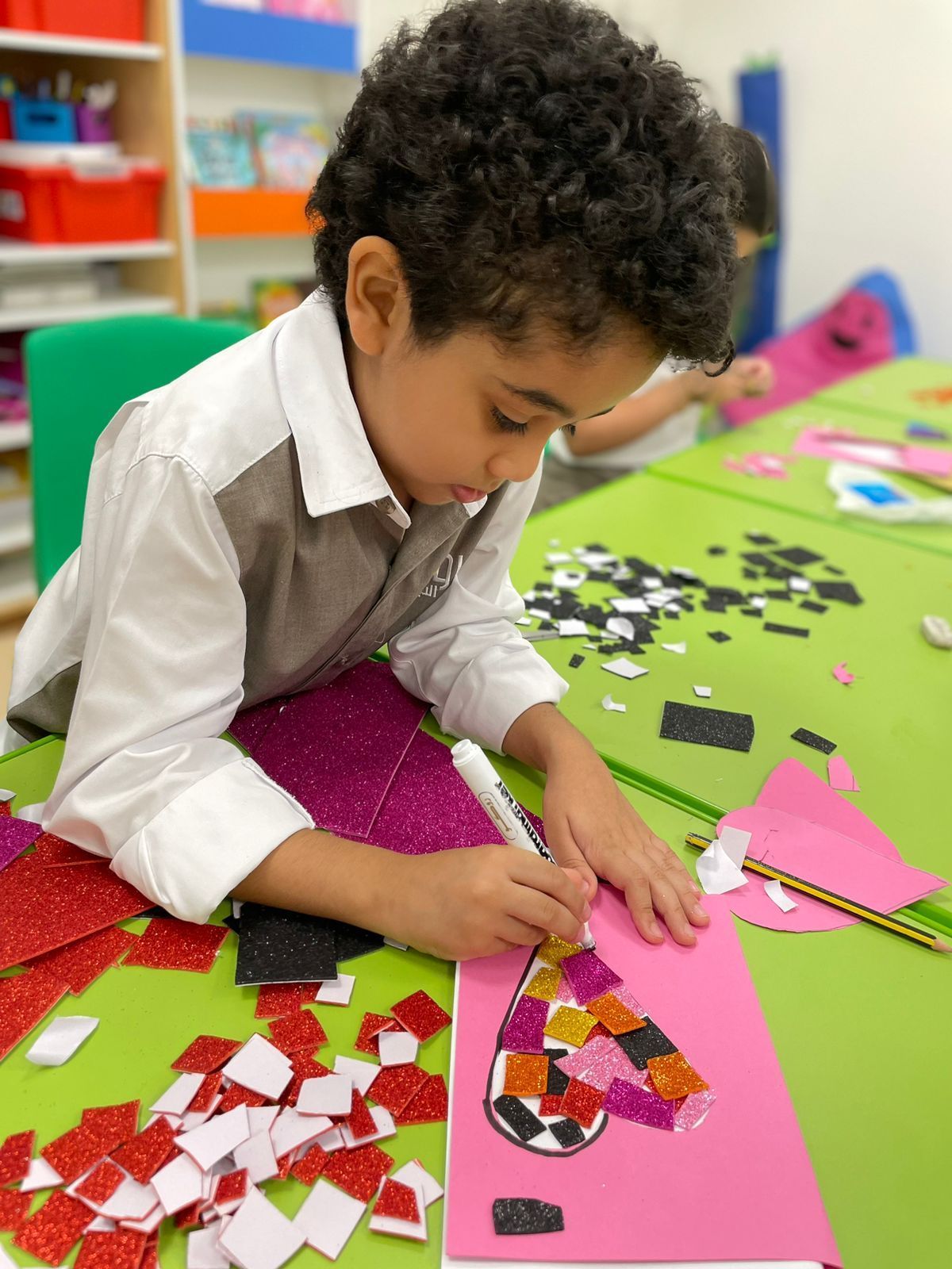 A young boy is sitting at a table making a heart out of paper