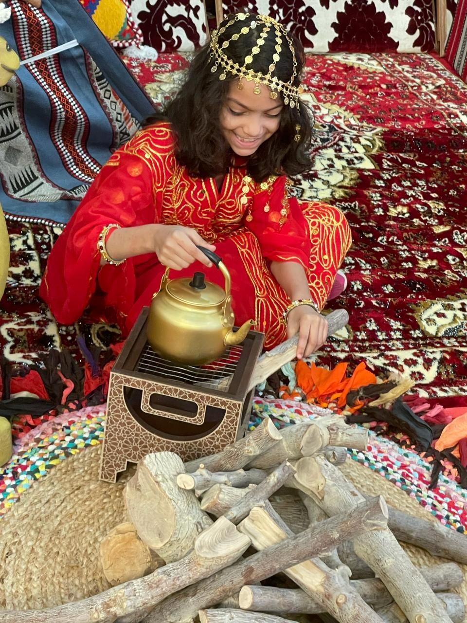 A girl in a red dress is sitting on the floor with a kettle.