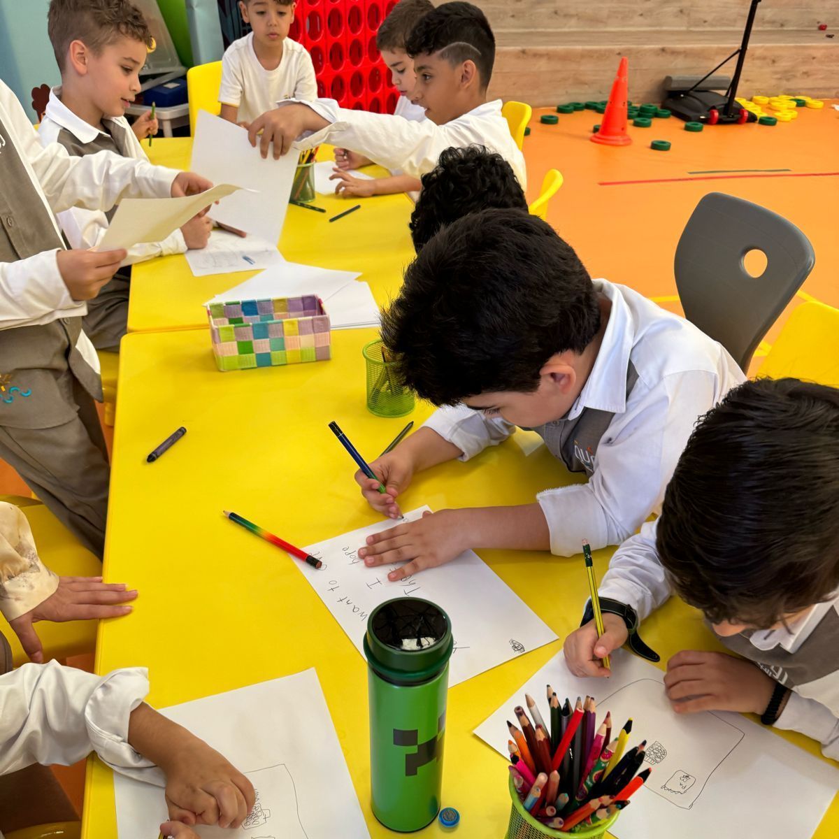 A group of children are sitting at a table with papers and pencils