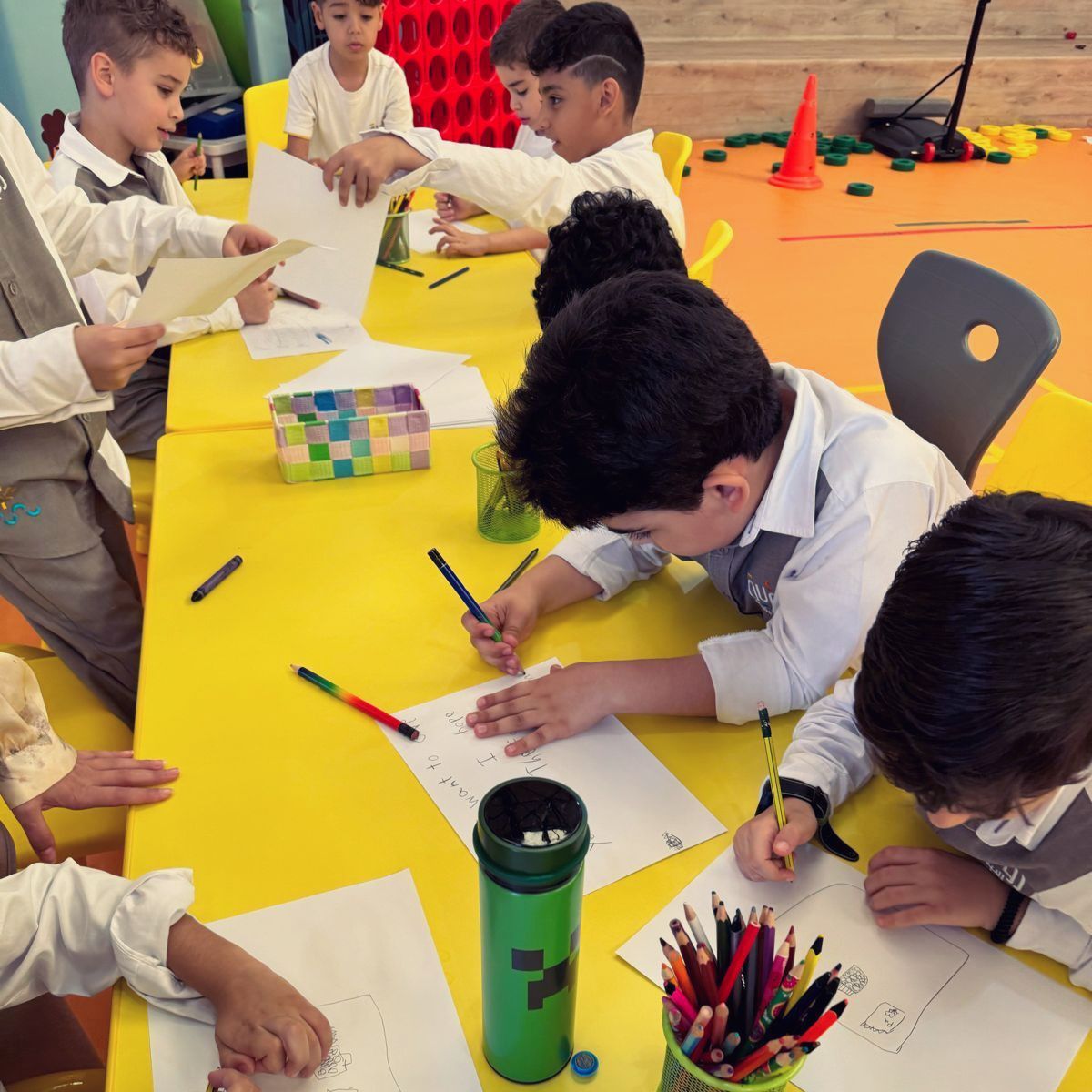 A group of young boys are sitting at a table drawing on papers