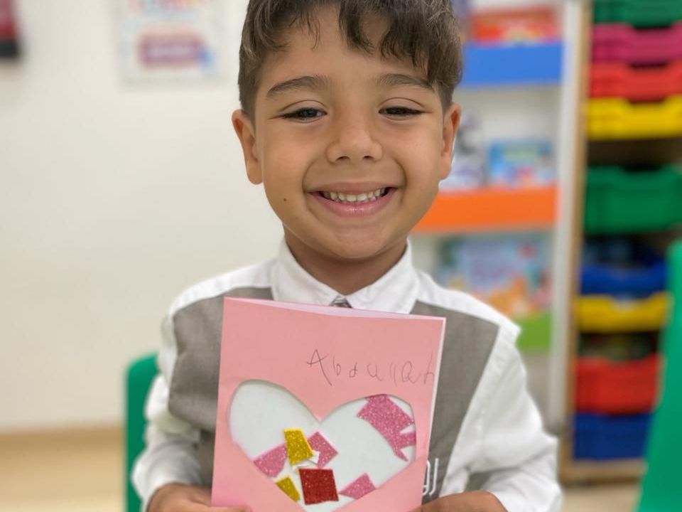 A young boy is holding a card with a heart on it and smiling.