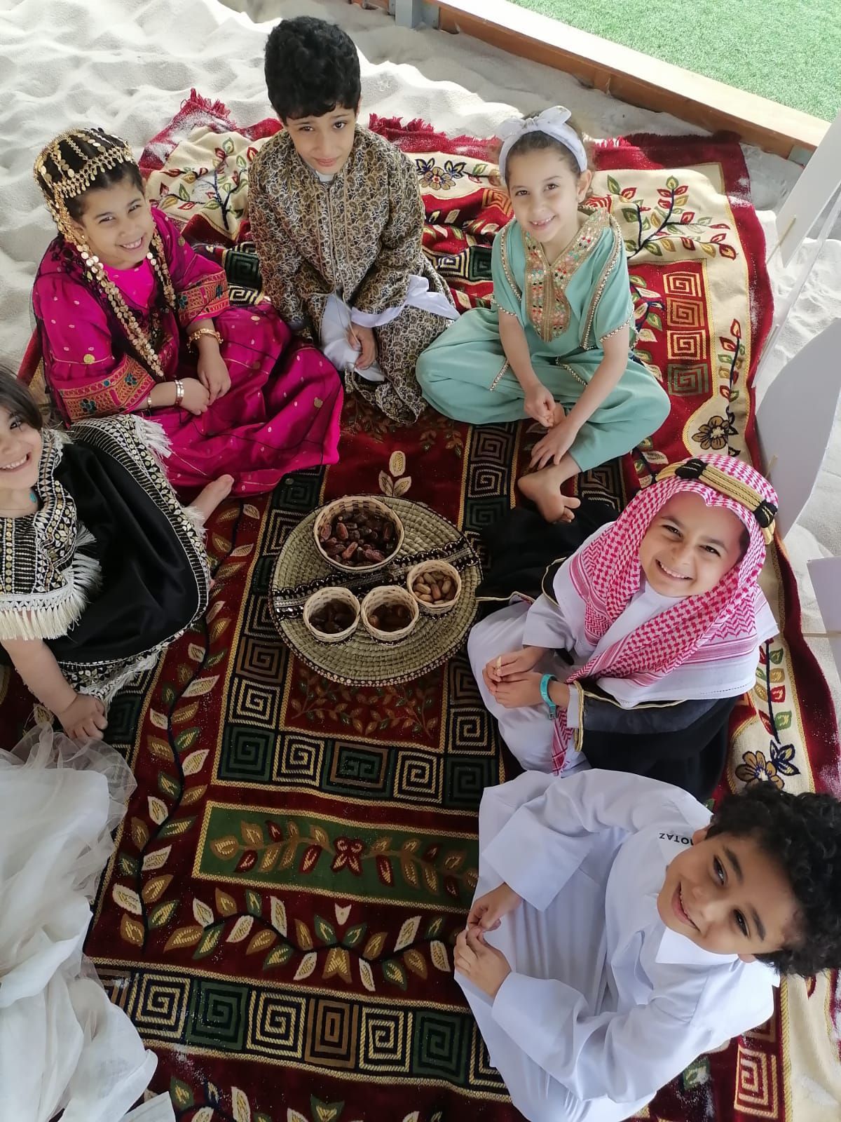 A group of children are sitting on a rug on the ground.