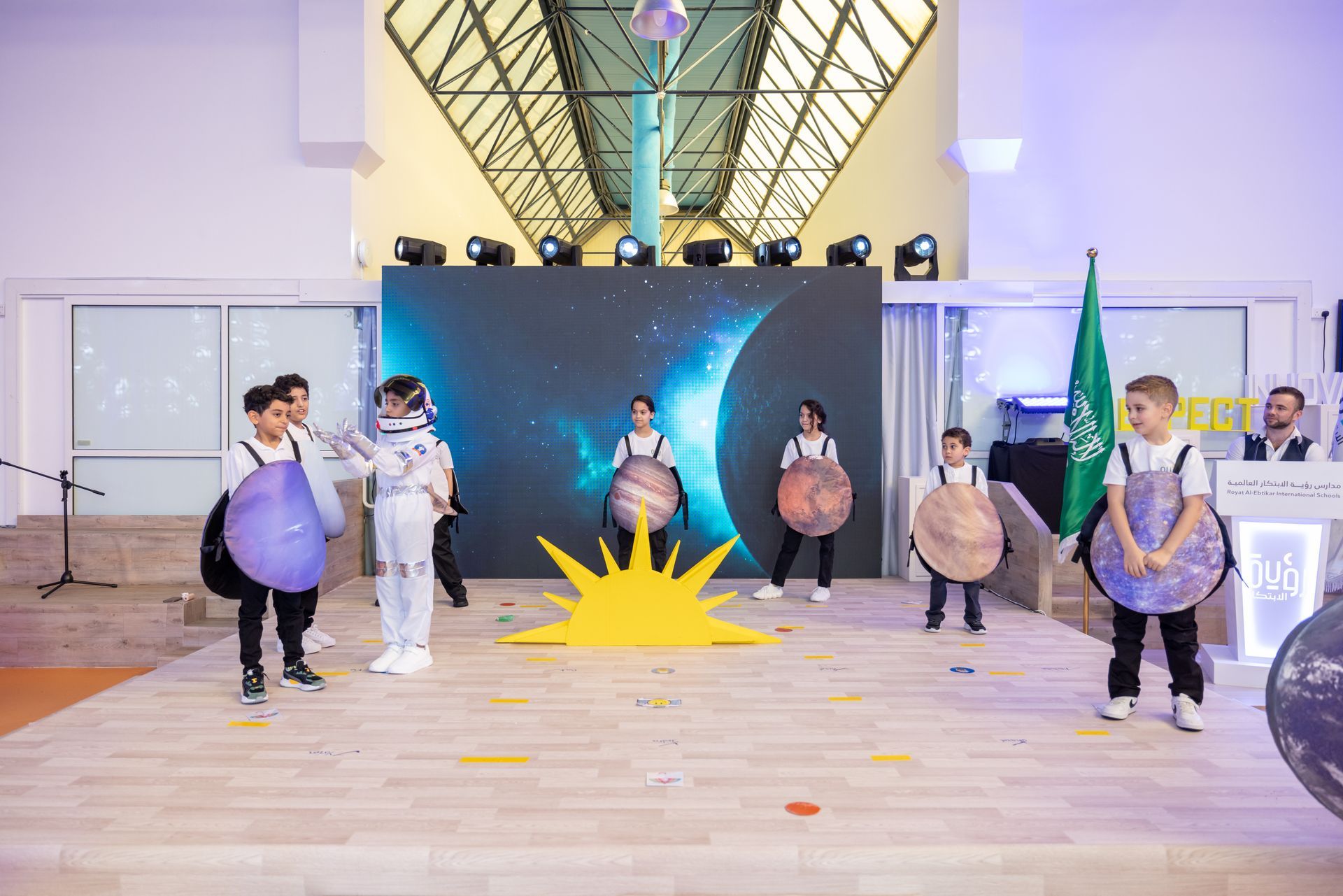 A group of children are standing on a stage in front of a large screen.