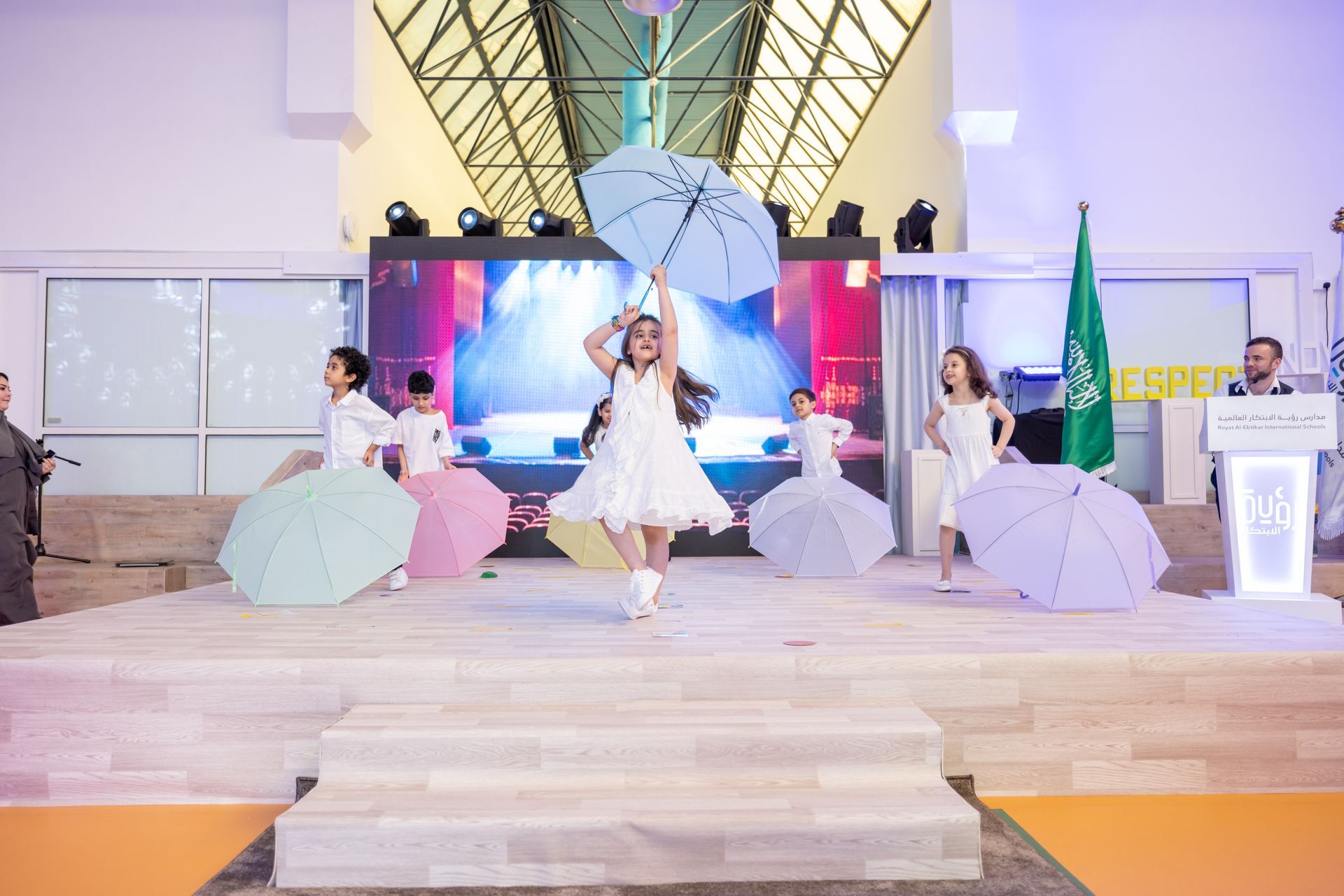 A group of young girls are dancing on a stage with umbrellas.