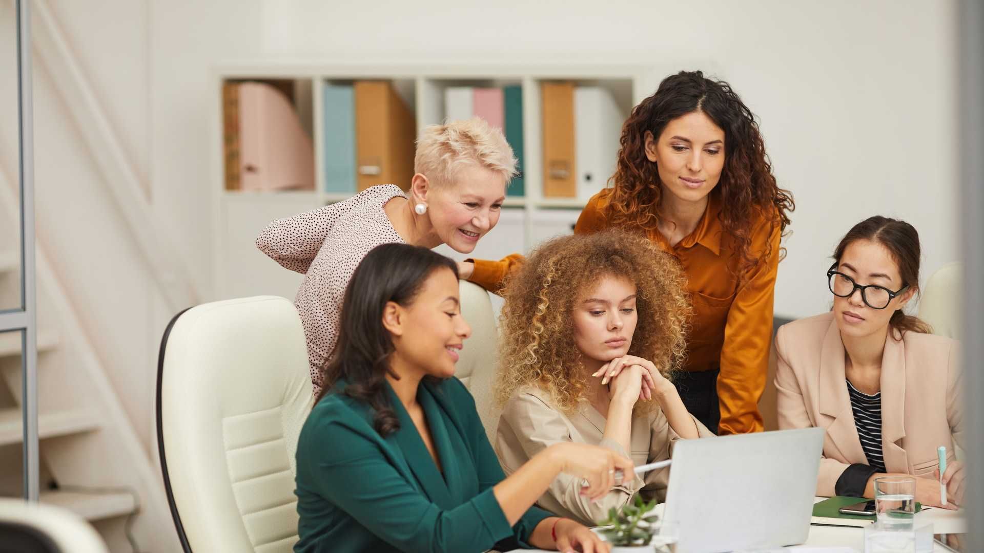 a group of office women discussing what is on the computer screen on the table