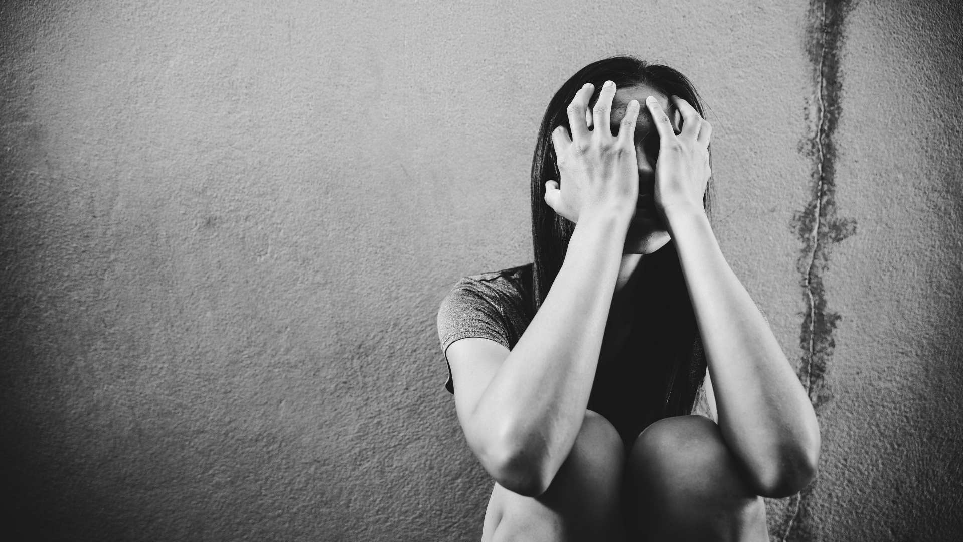 black and white photo of a woman covering face with both of her hands traumatized