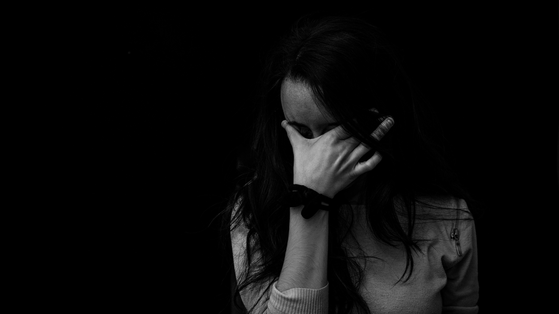 black and white photo of girl covering her eyes with one hand crying