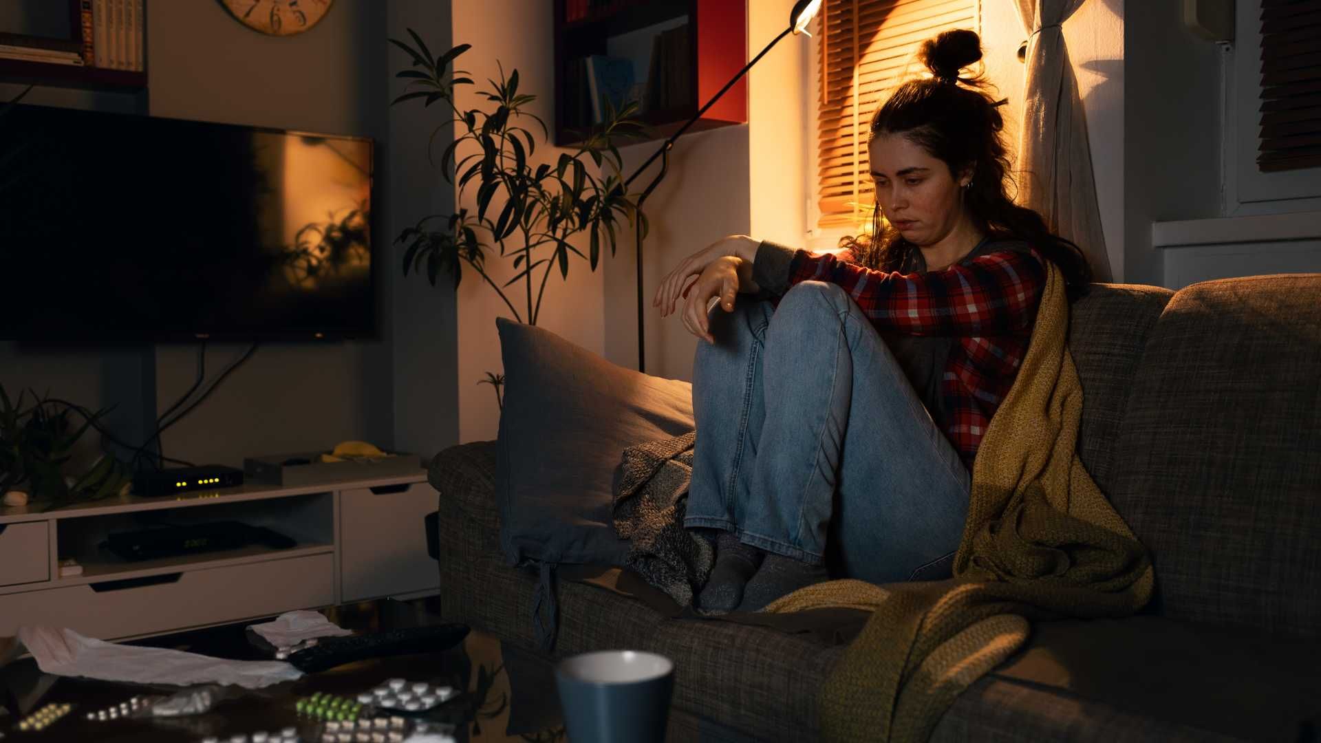 depressed teen home alone sitting on her sofa at home in a dark living room