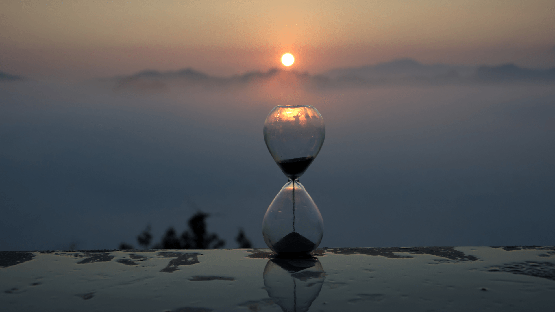 hourglass on top of a puddle with sun setting on the background