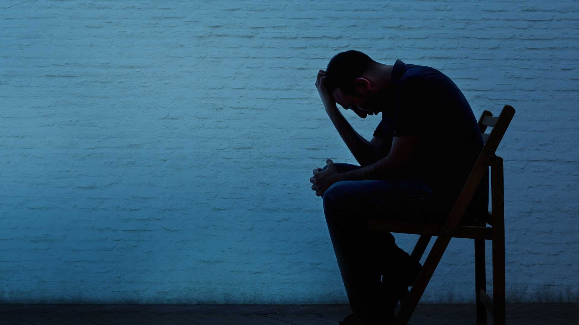 silhouette of a man sitting on a chair  holding his head down with one hand