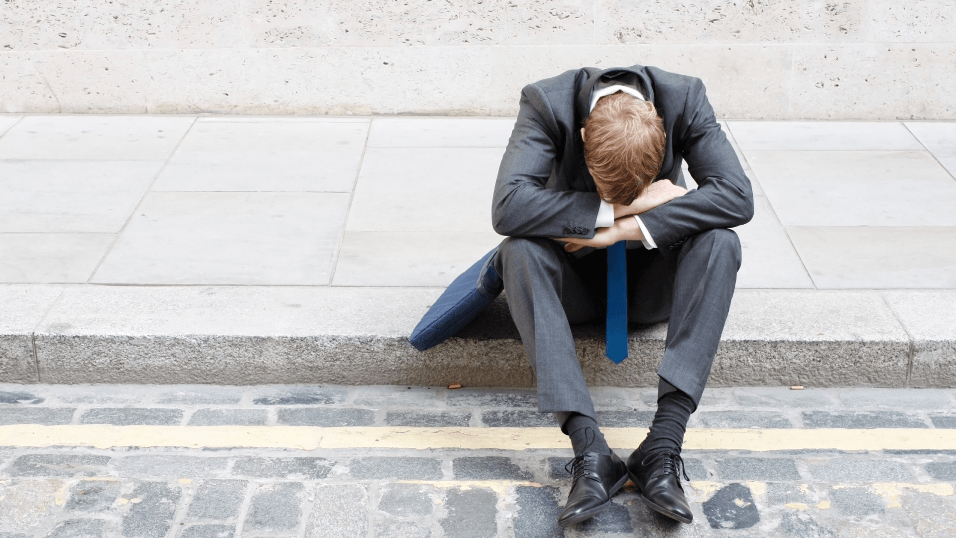 man on a suit sitting on the curb curled up