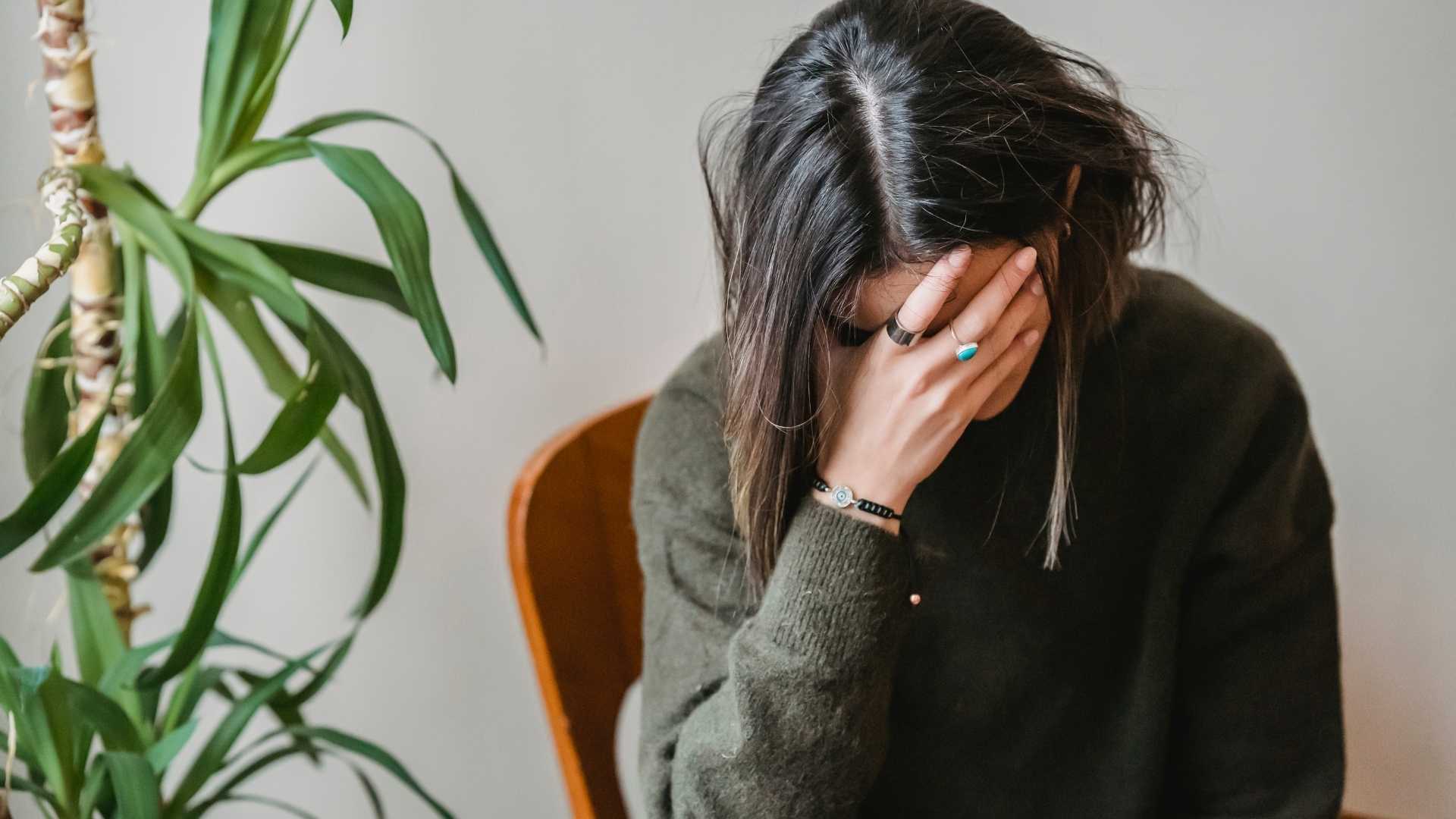 woman sitting on a chair with her head down and right palm on her face