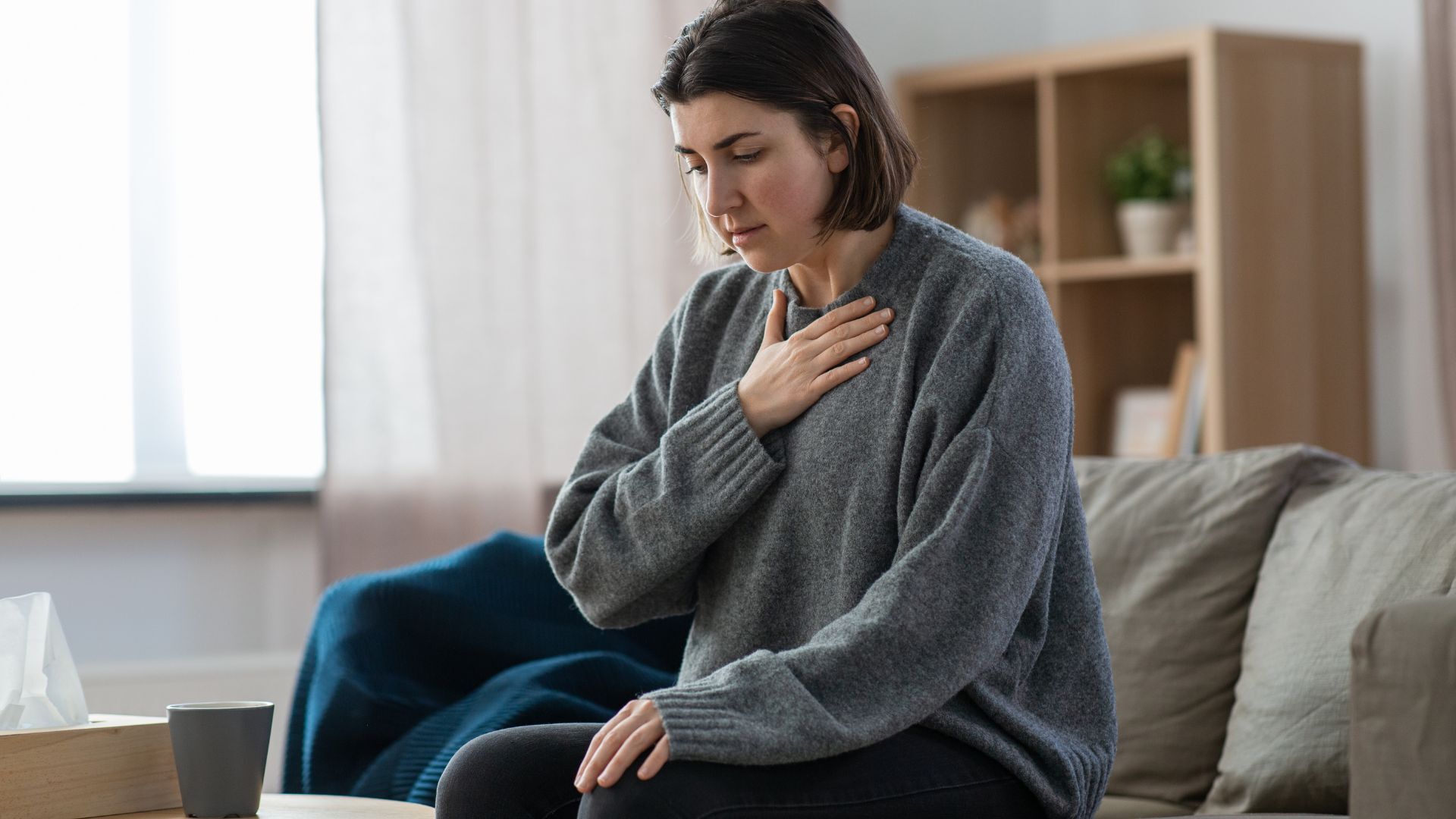 woman sitting on the couch alone with her hand on her chest having a panic attack