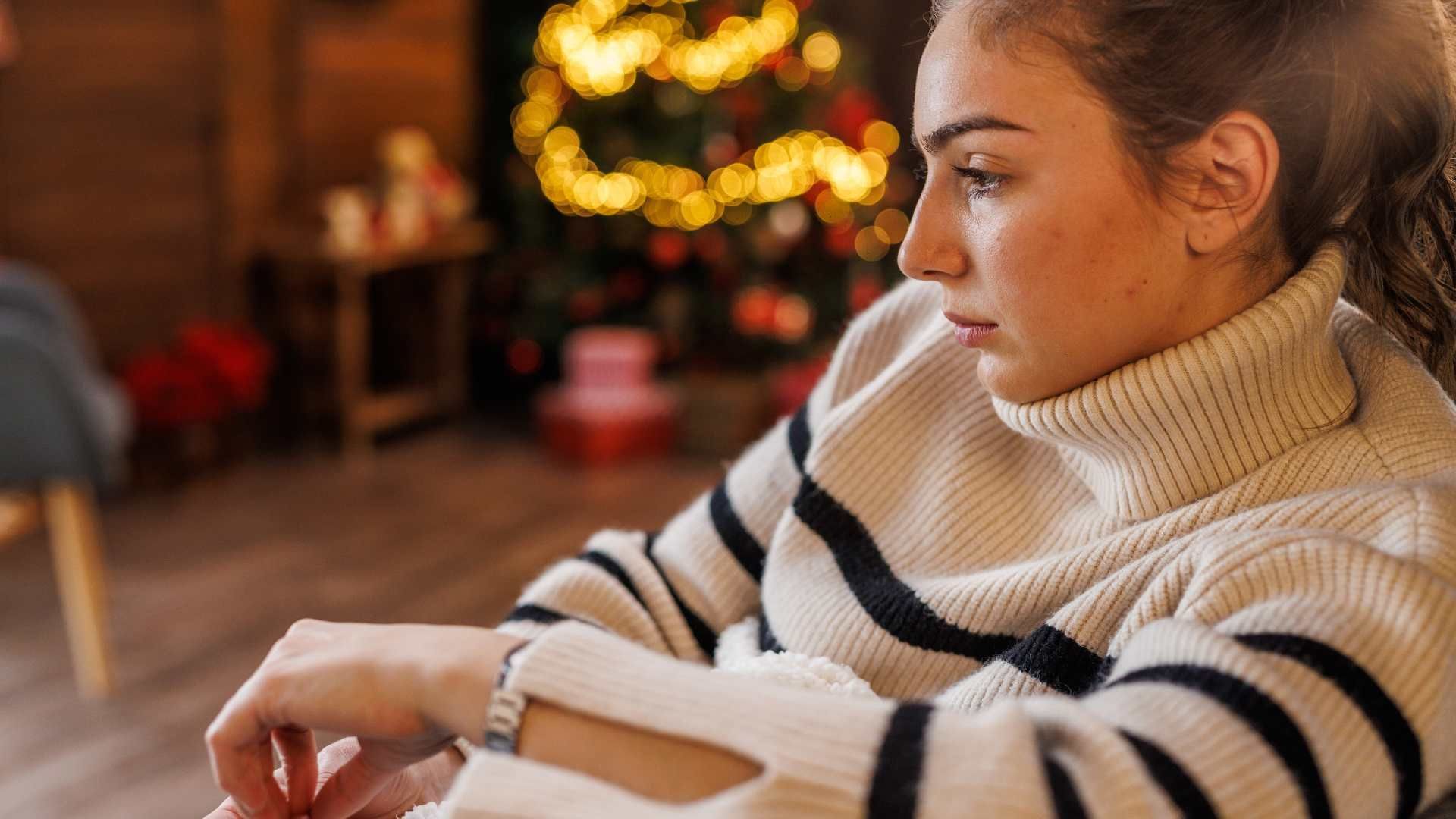 woman sitting alone at home beside her light up christmas tree