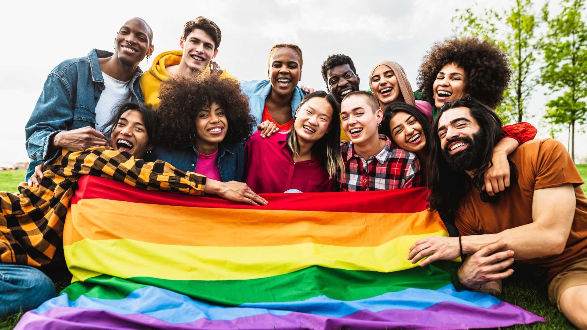 a group of young adults holding one big rainbow flag