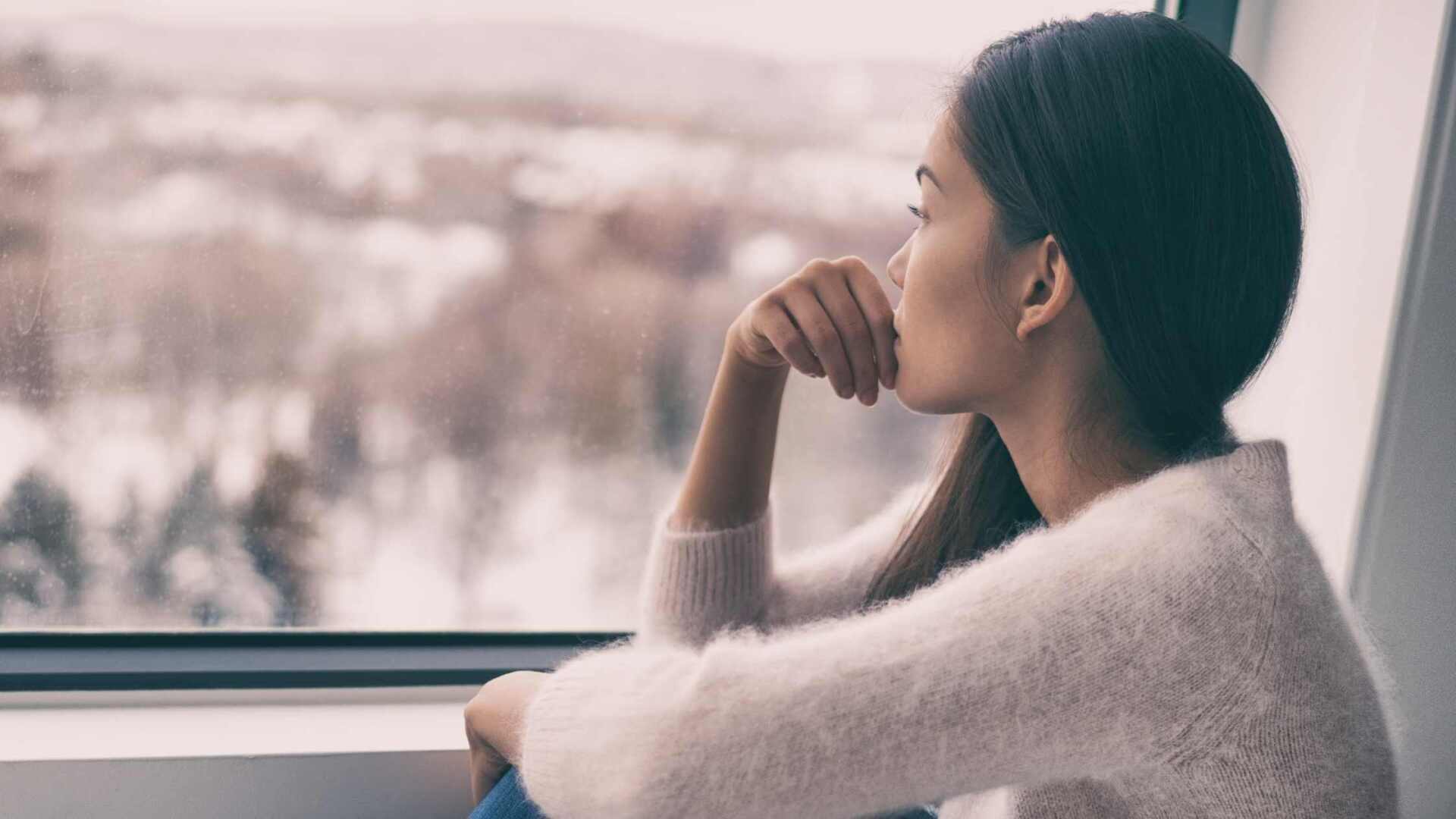 woman looking out of the window from the inside of the house