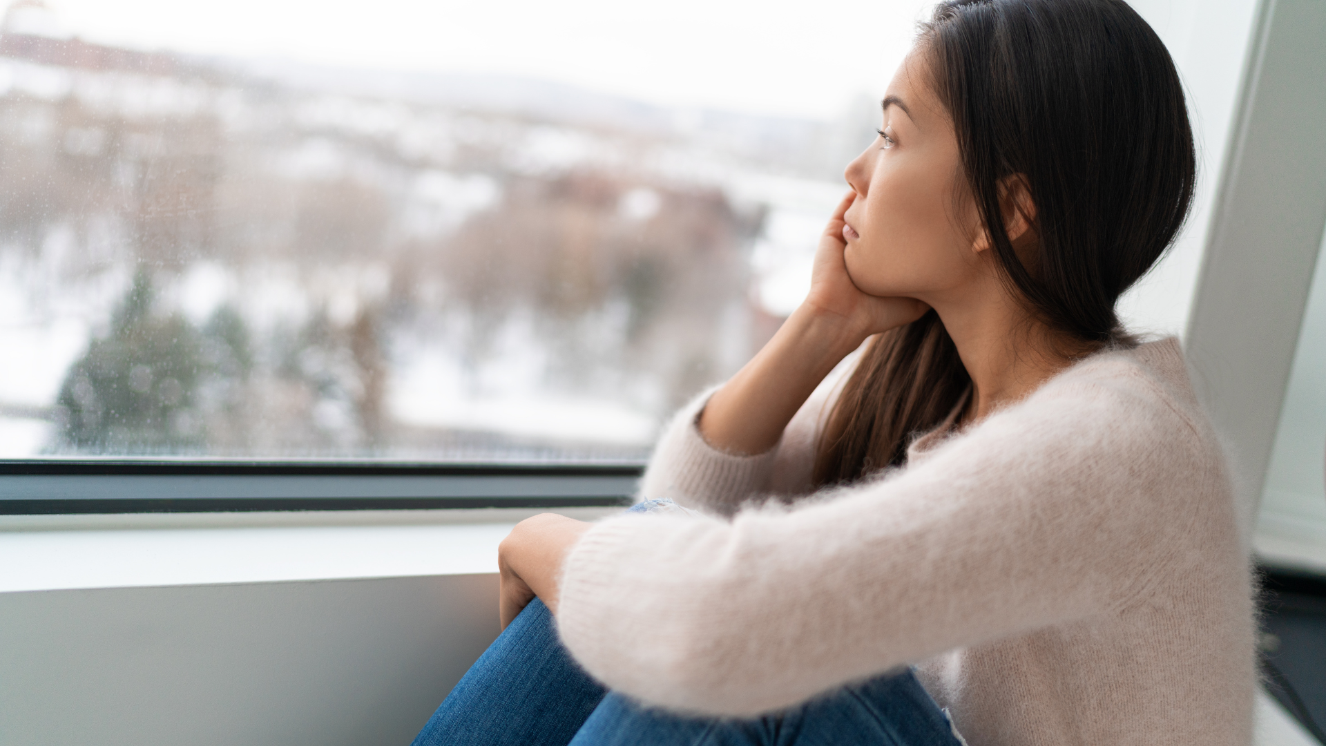 women inside with her hand on her face looking outside the glass window