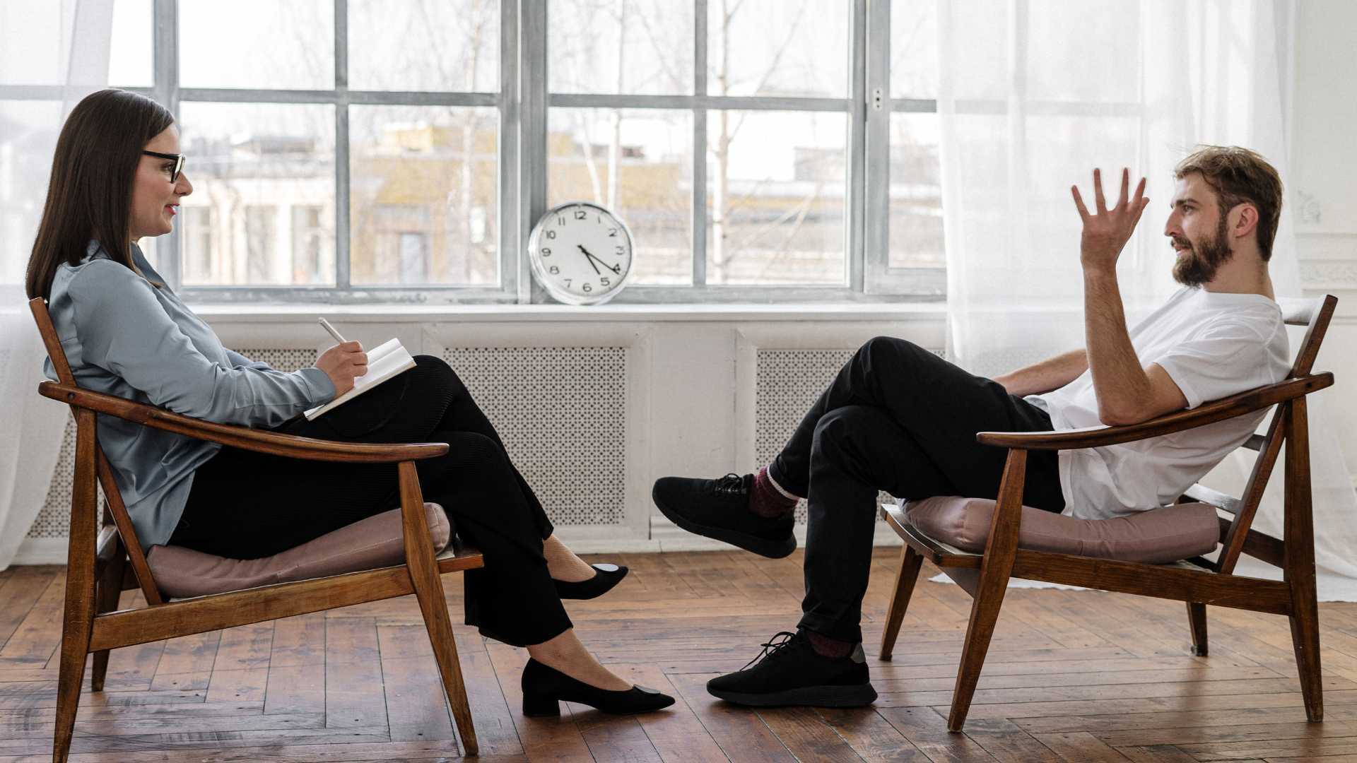 man sitting on a chair with his hands up as he speaks to his therapist sitting on a chair in front of him