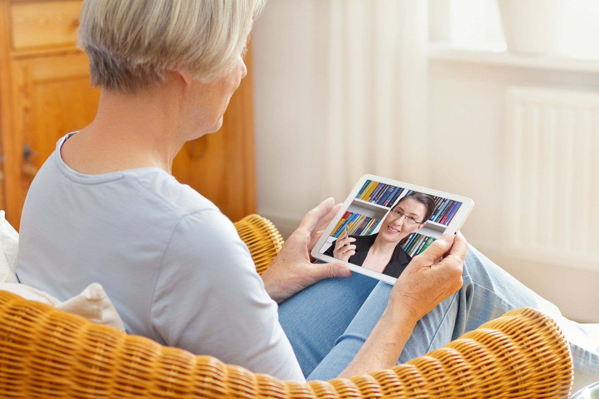 Elderly woman sitting on a couch holding a tablet while speaking to her tharapist virtually