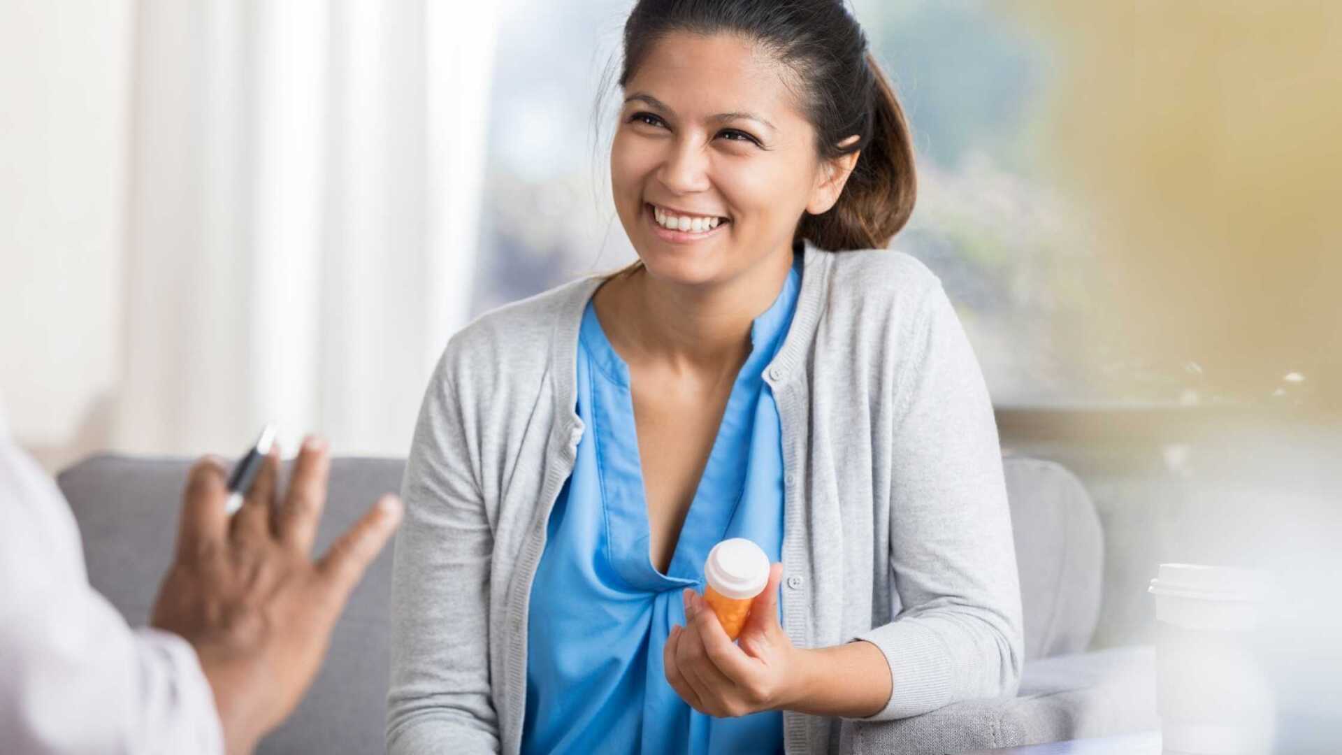 female smiling holding a prescription bottle listening to her doctor explaining