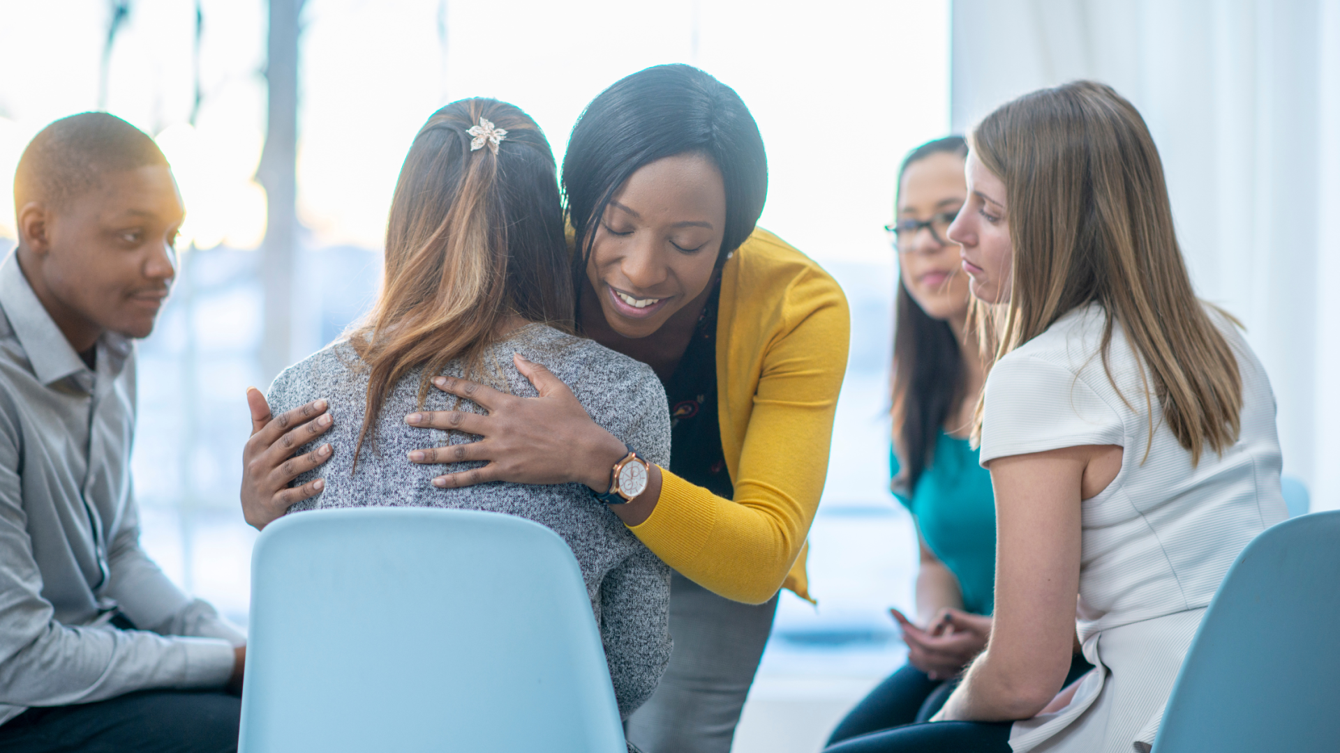 group of people sitting on a chair facing one another in a circle one girl comforting another girl 