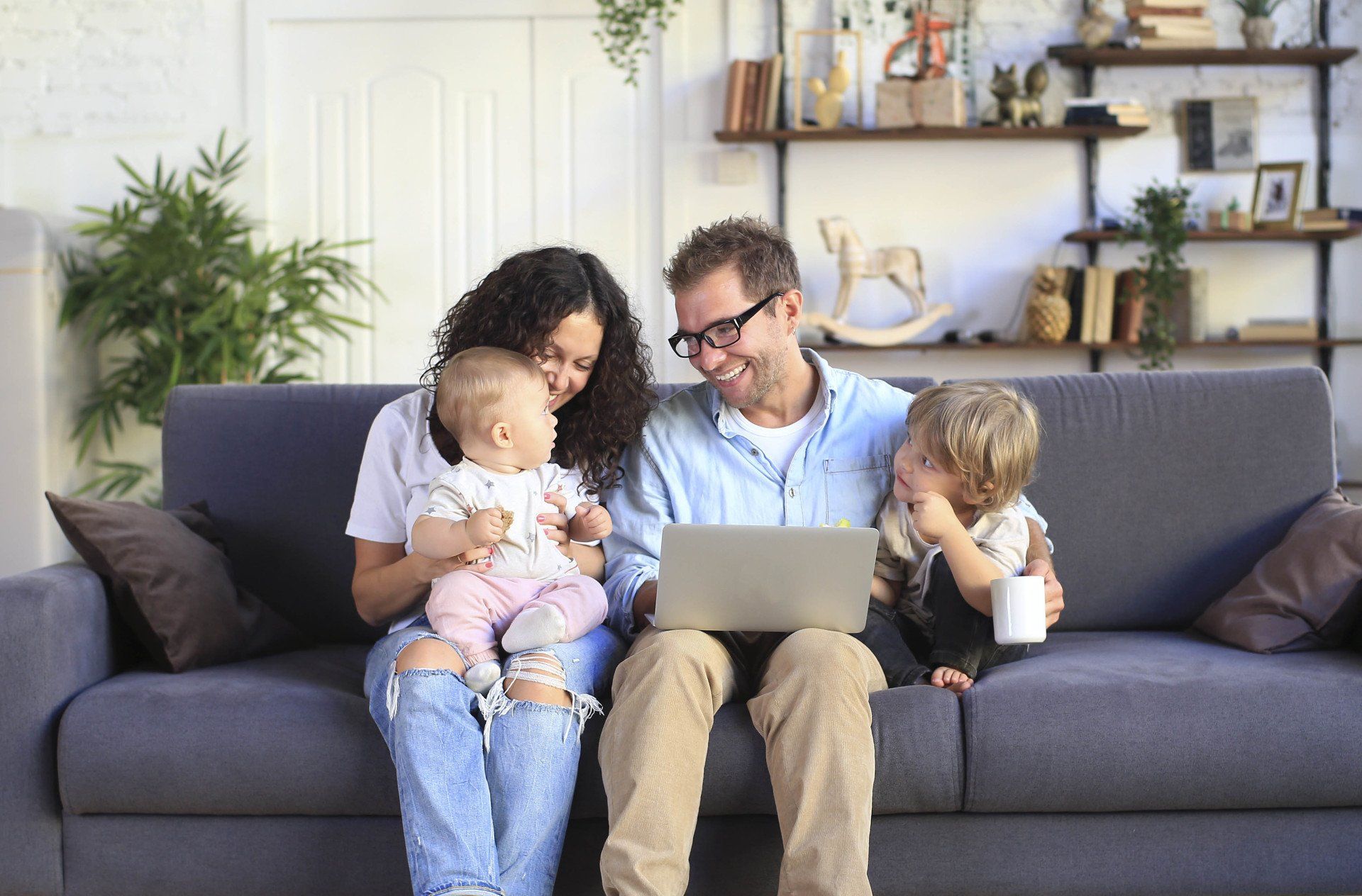 man and woman on the sofa with their kids ages 0 to 3. Man has laptop on his lap booking an appointment.