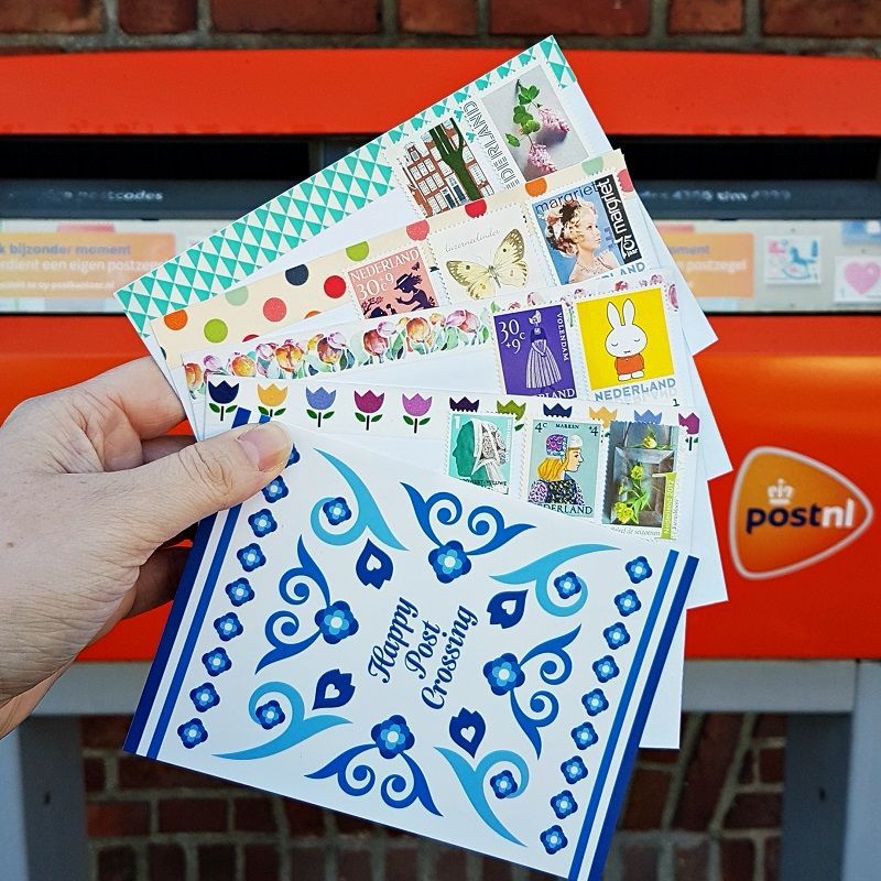 Een Nederlandse brievenbus met op de voorgrond een aantal verschillende kaarten voor postcrossing