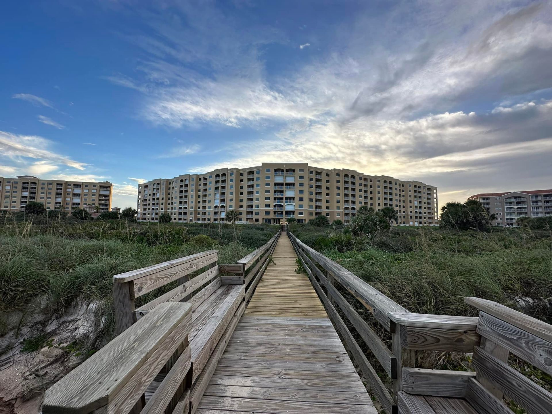 Wooden boardwalk leads to beachfront condos under a cloudy sky.