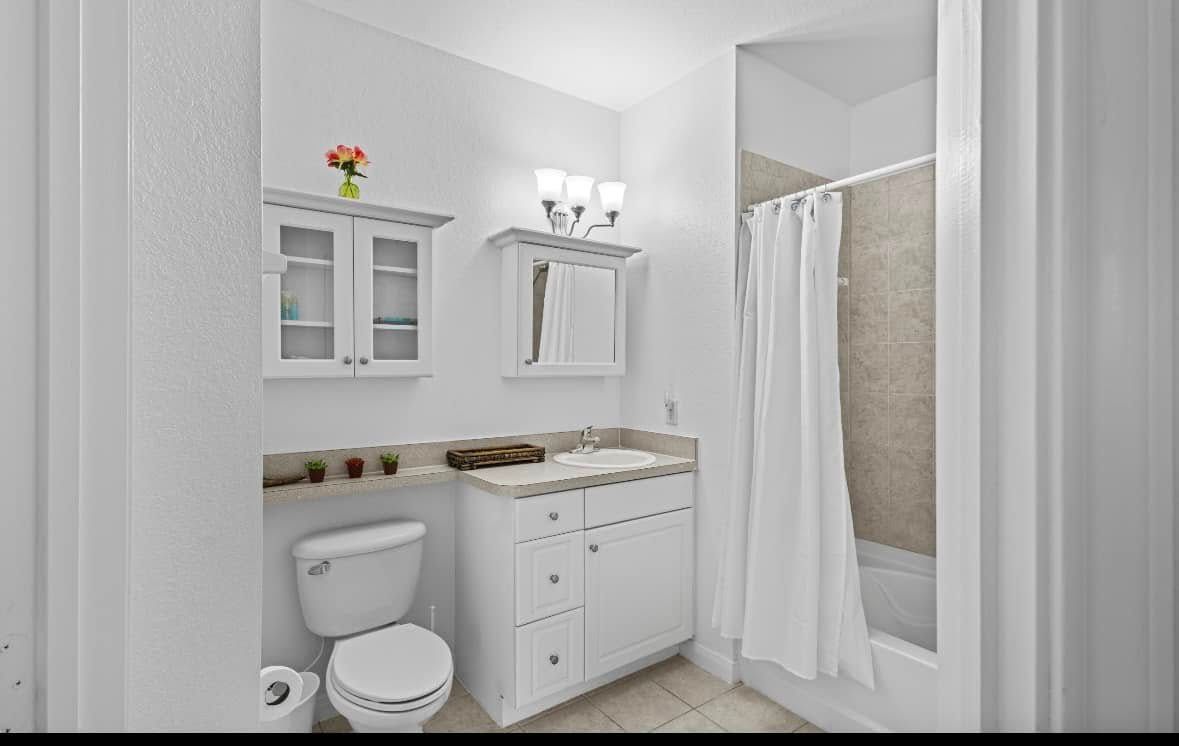 White bathroom with a toilet, vanity, and shower. Small cabinet and mirror above vanity.