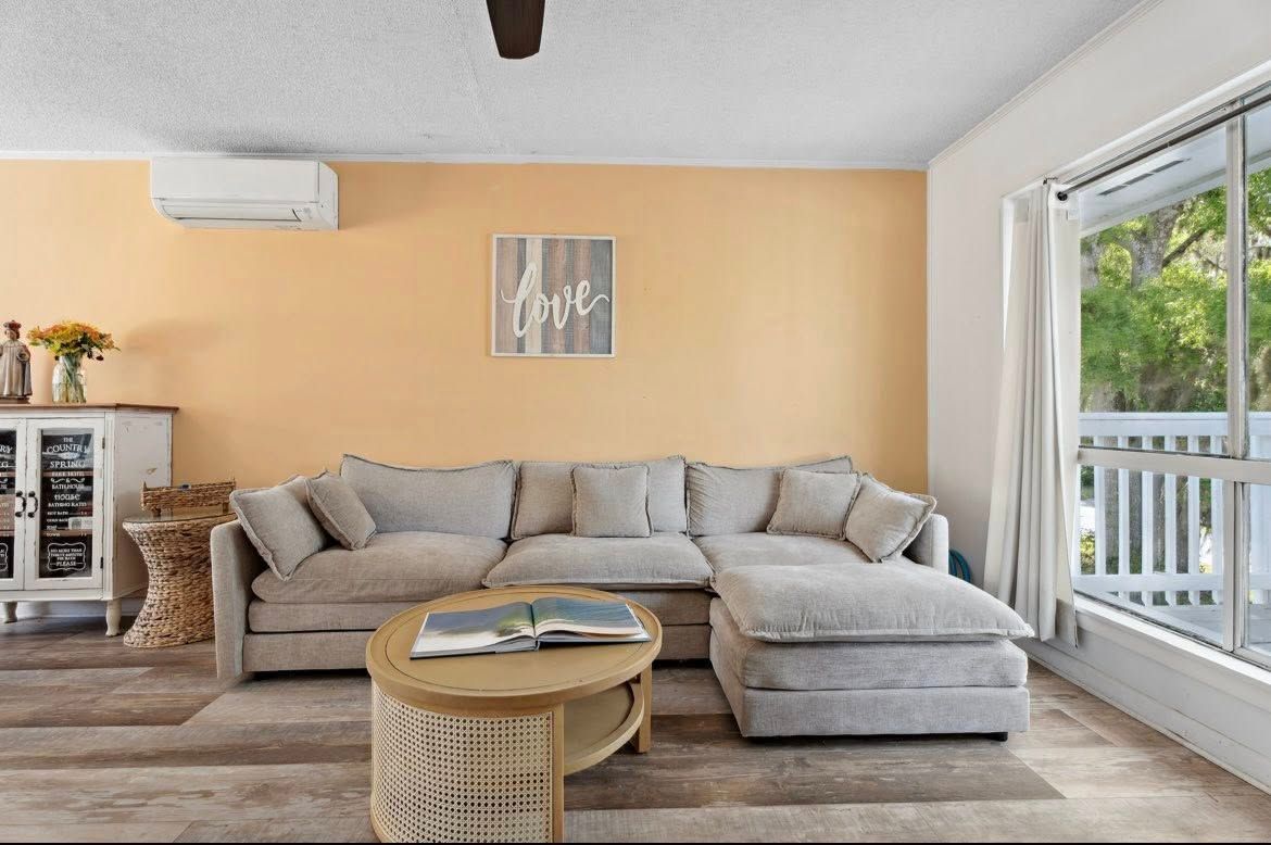 Living room with beige sectional sofa, coffee table, and peach-colored walls. A window is on the right.