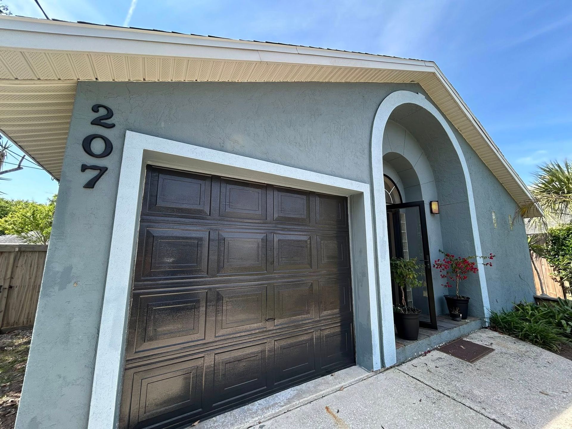 Gray house with black garage door, arched doorway, and the number 207.