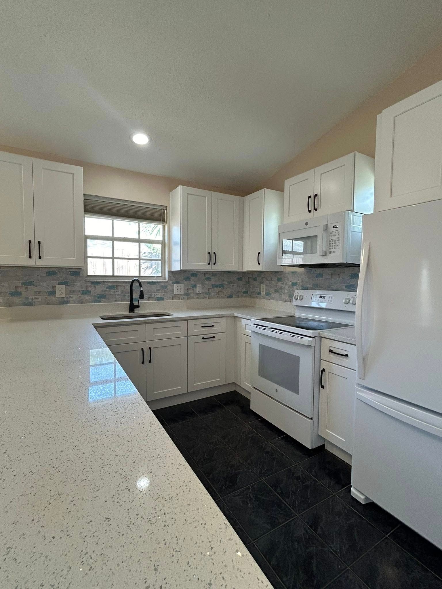 White kitchen with white cabinets, speckled countertops, and a black floor.
