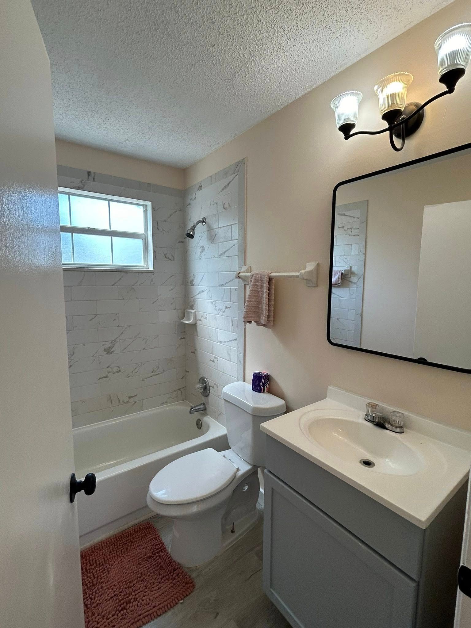 Bathroom with tub, toilet, and sink. Pink walls, gray vanity, and black framed mirror.