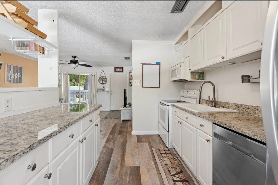 White kitchen with granite countertops, stainless steel appliances, and wood-look flooring.