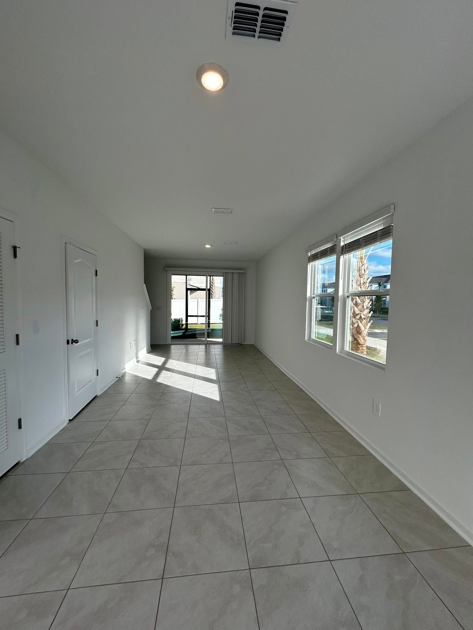 Empty room with tiled floor, white walls, two windows, and door to outside.